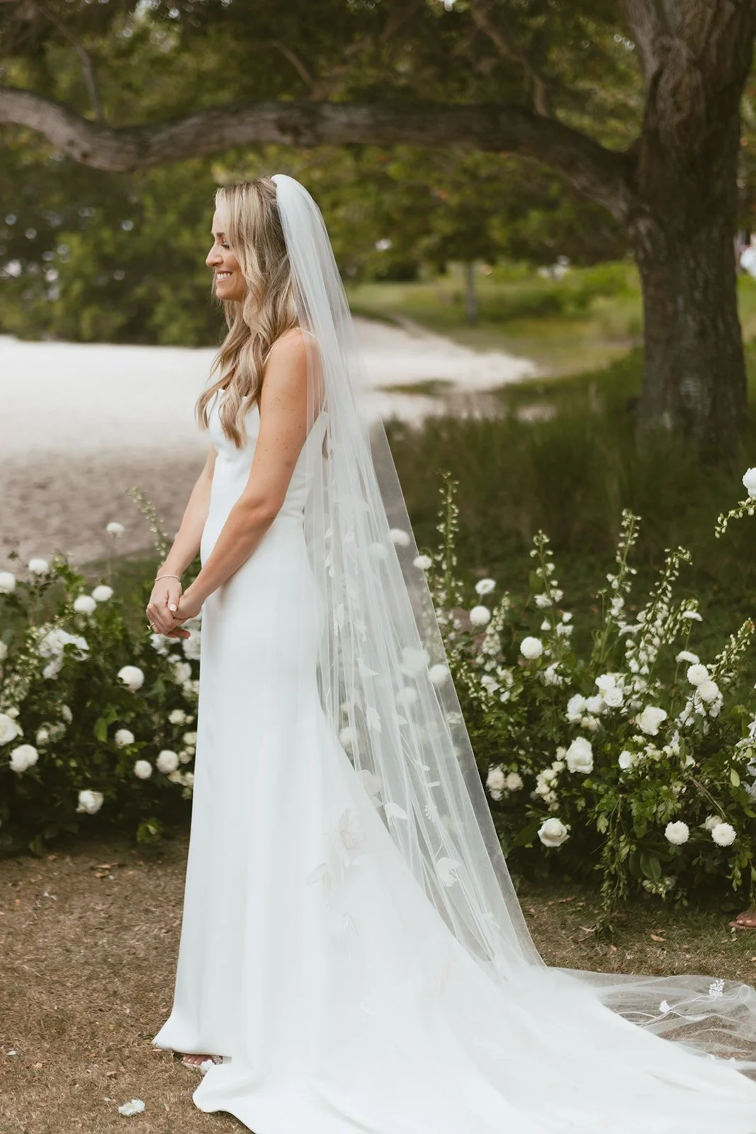 Bride in a long veil beside the white ground meadow of roses and stock