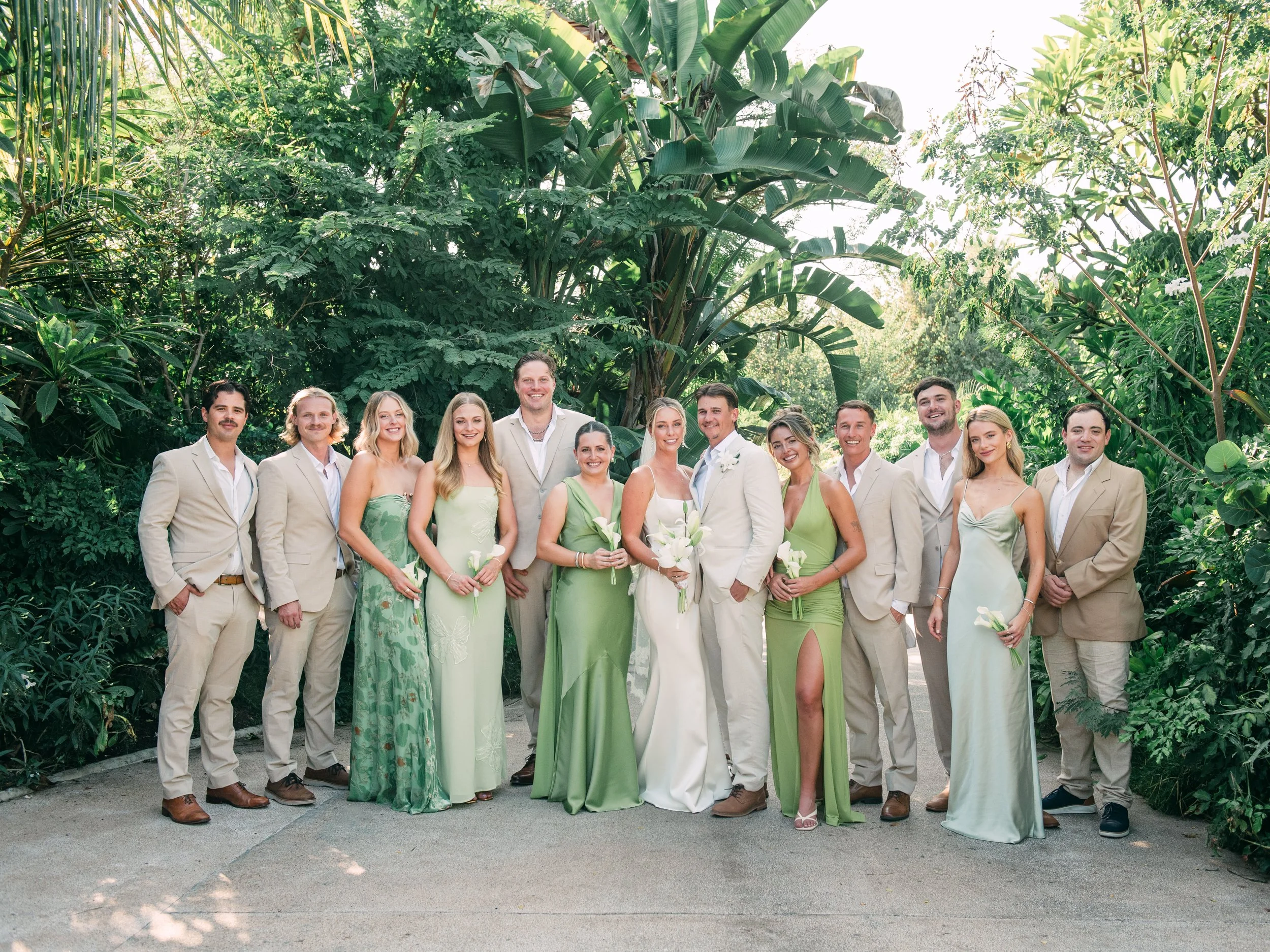 Full wedding party in green and cream beneath banana palms at W Punta de Mita