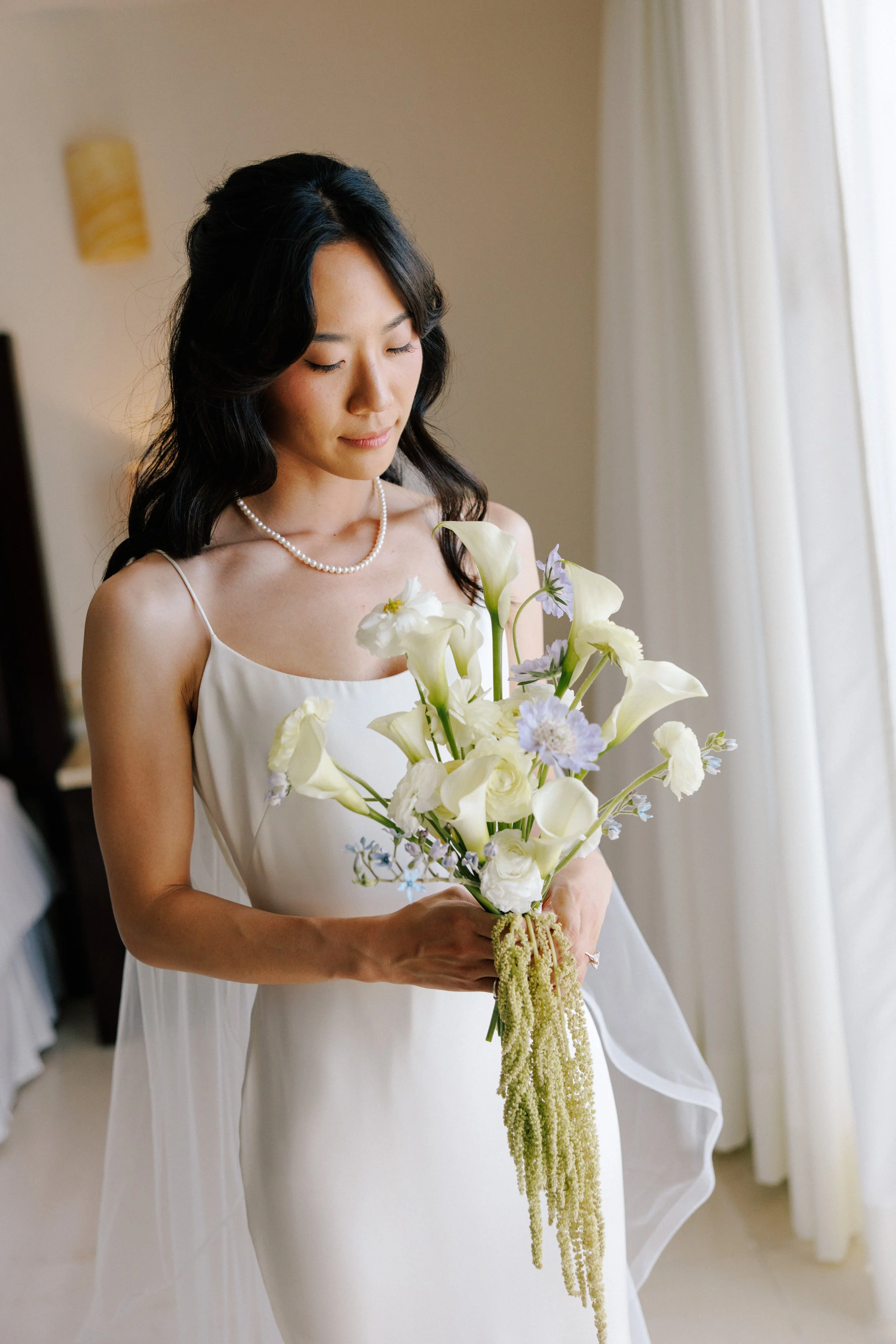 Bride holding her white calla bouquet in window light at Grand Miramar, Puerto Vallarta