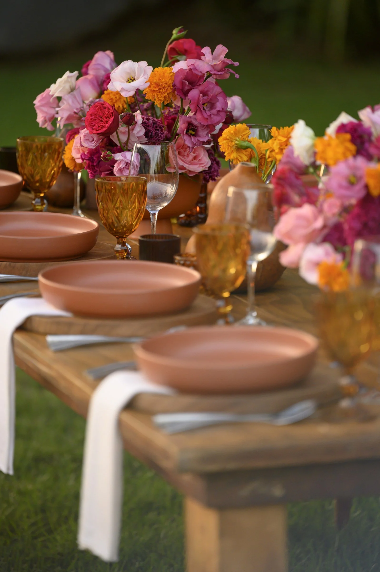 Long table with repeating compotes of magenta blooms and terracotta place settings
