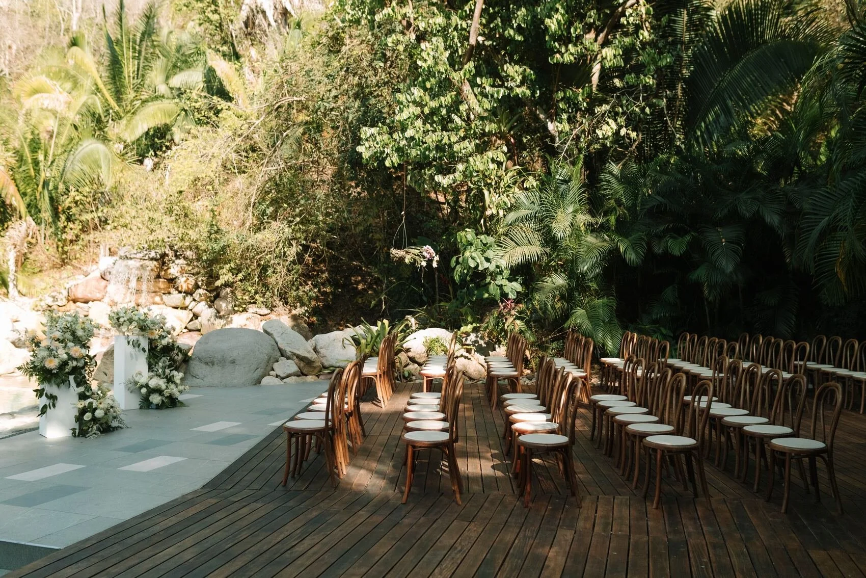 eremony set against the waterfall with bentwood chairs and white pedestal florals at Garza Blanca The Forum