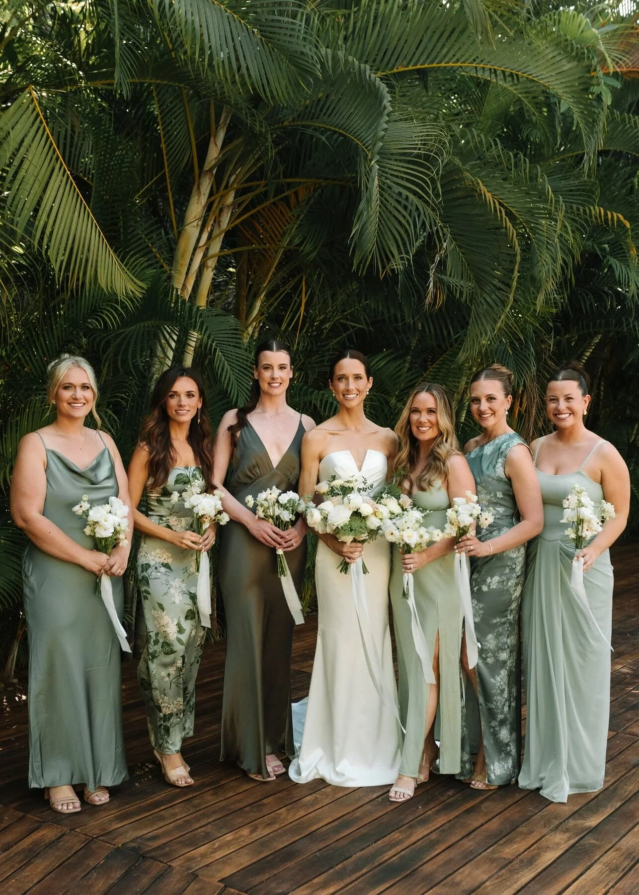 Bridesmaids in sage green holding white garden bouquets under the palms at Garza Blanca