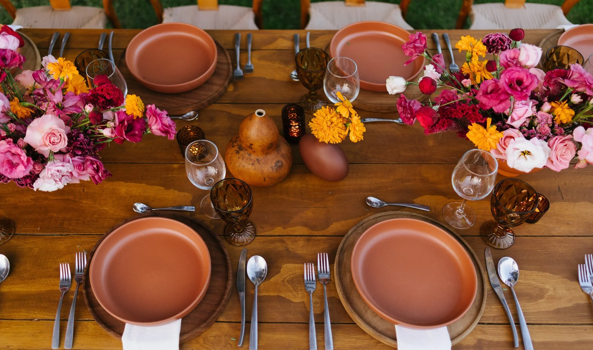 Marigold and magenta placed down the center of a bare wood table, seen from above