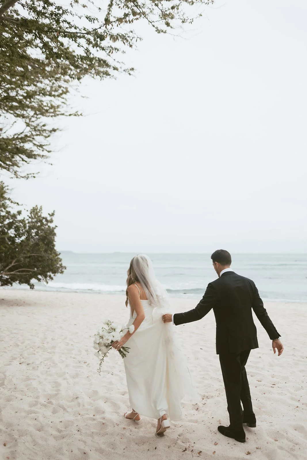 Bride and groom walking the beach at St. Regis Punta Mita, bouquet in hand