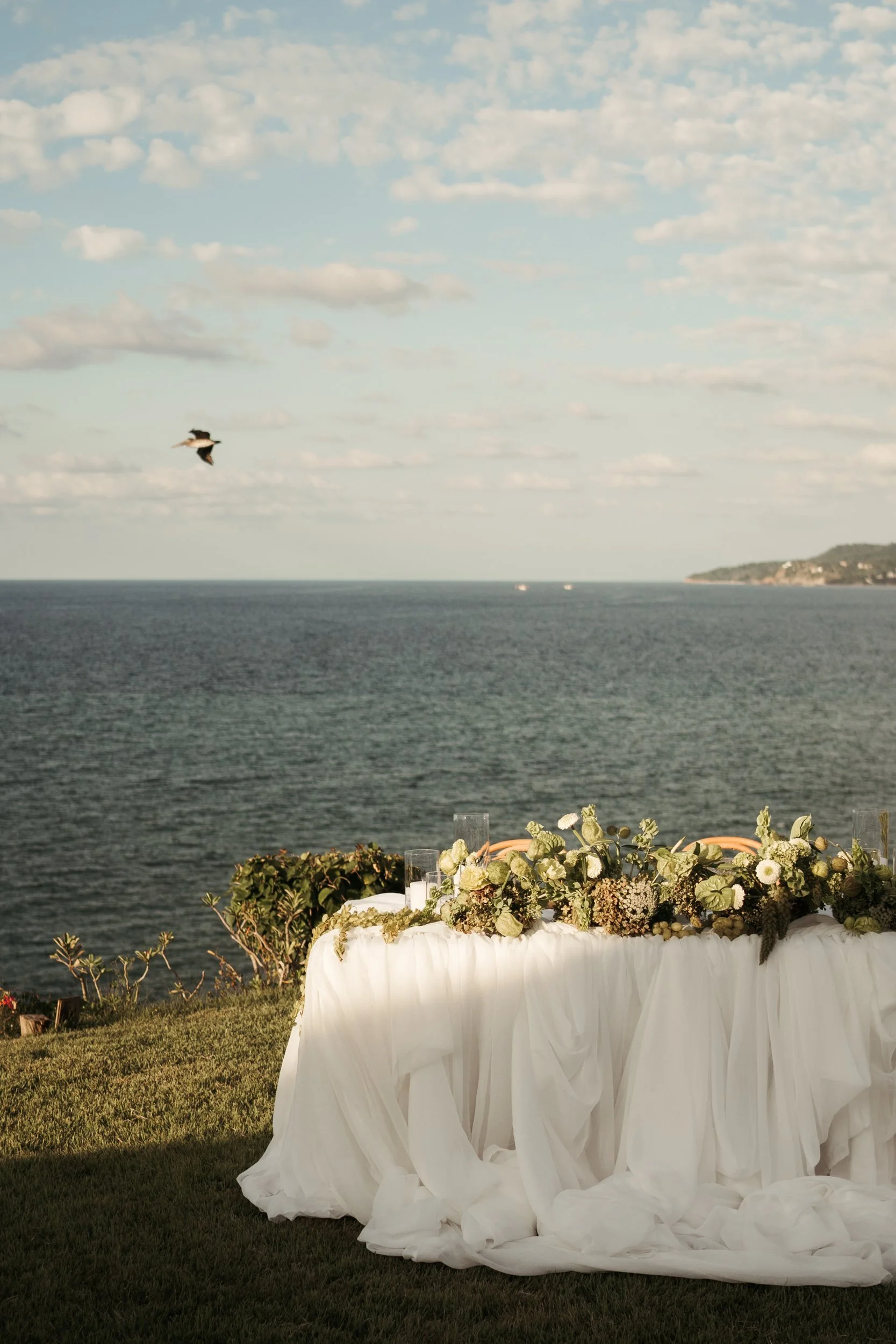 Sweetheart table in white draping topped with a green and white garland, Pacific behind, Sayulita