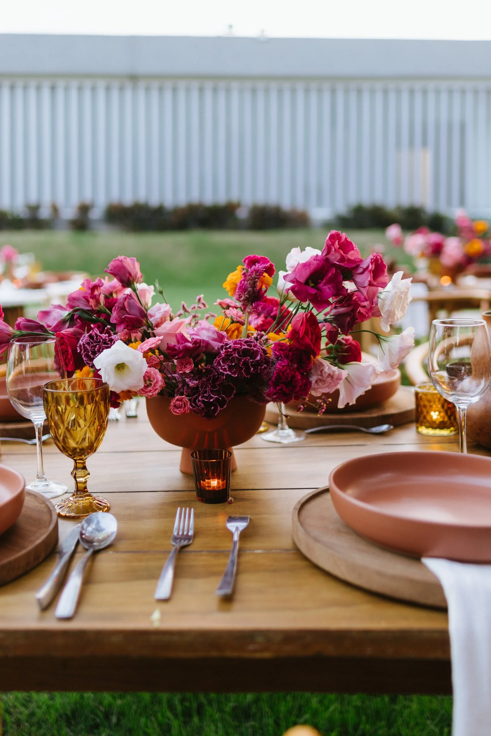 Magenta and coral centerpiece on a bare wood table at a Mexican wedding