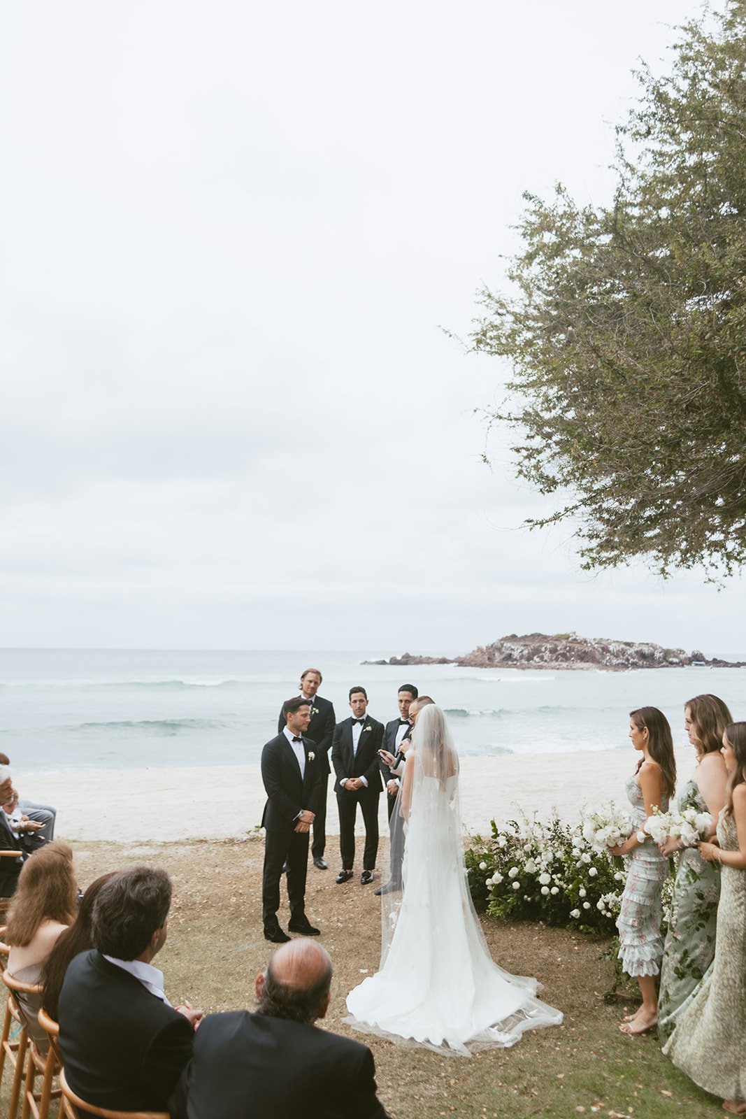 Beach ceremony facing the Pacific with grounded white florals at the altar