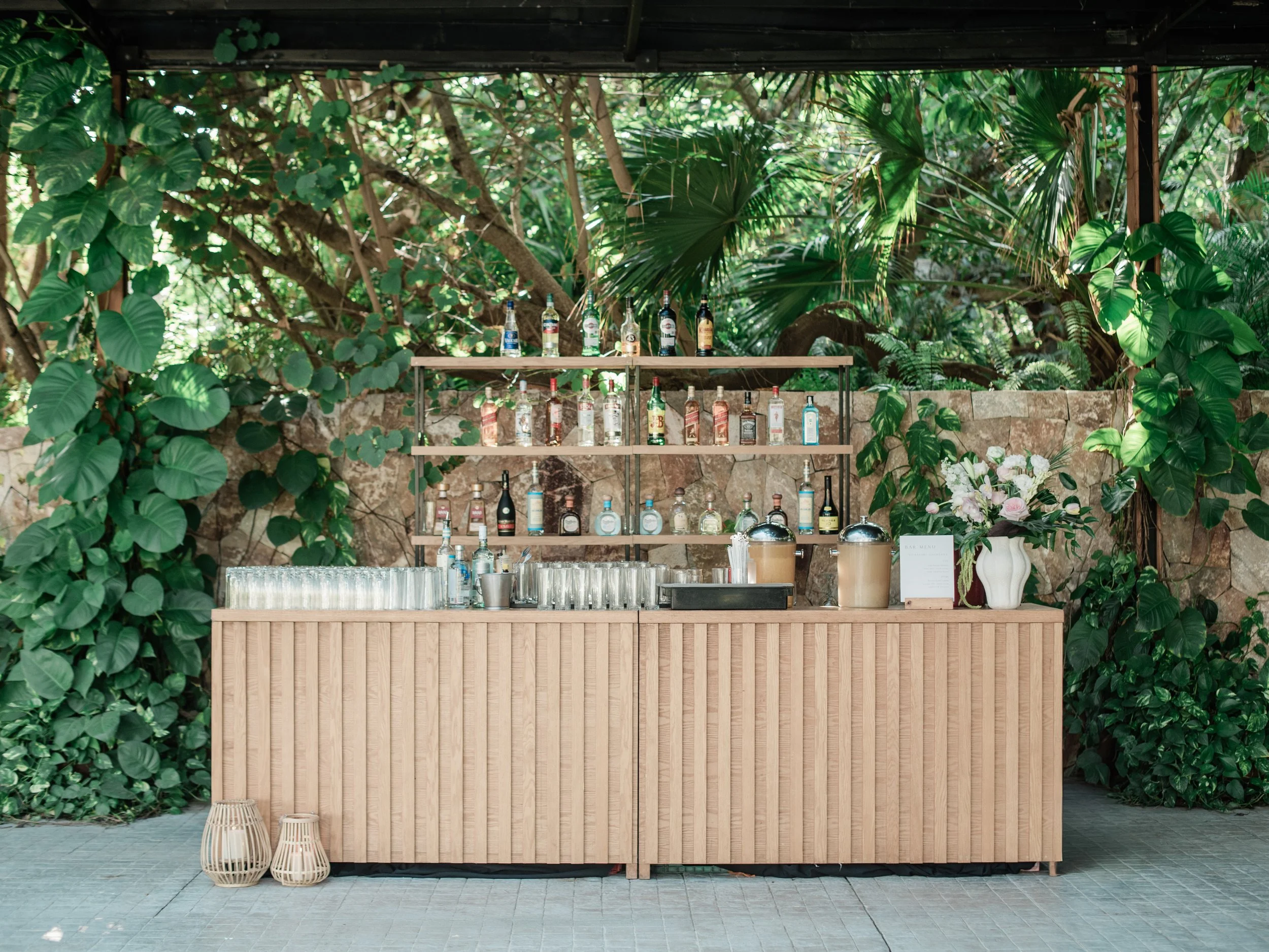 Wooden bar with a white rose arrangement against stone and foliage at W Punta de Mita