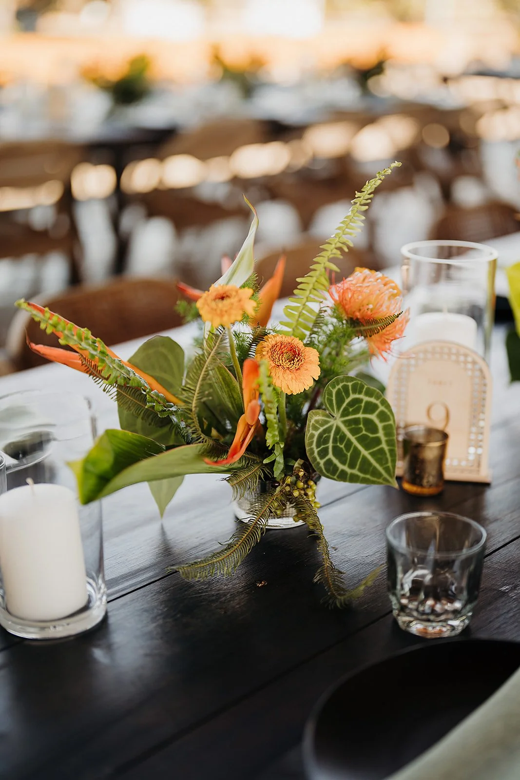 Centerpiece of orange mini gerbera and tropical foliage at Tierra Tropical Polo Club