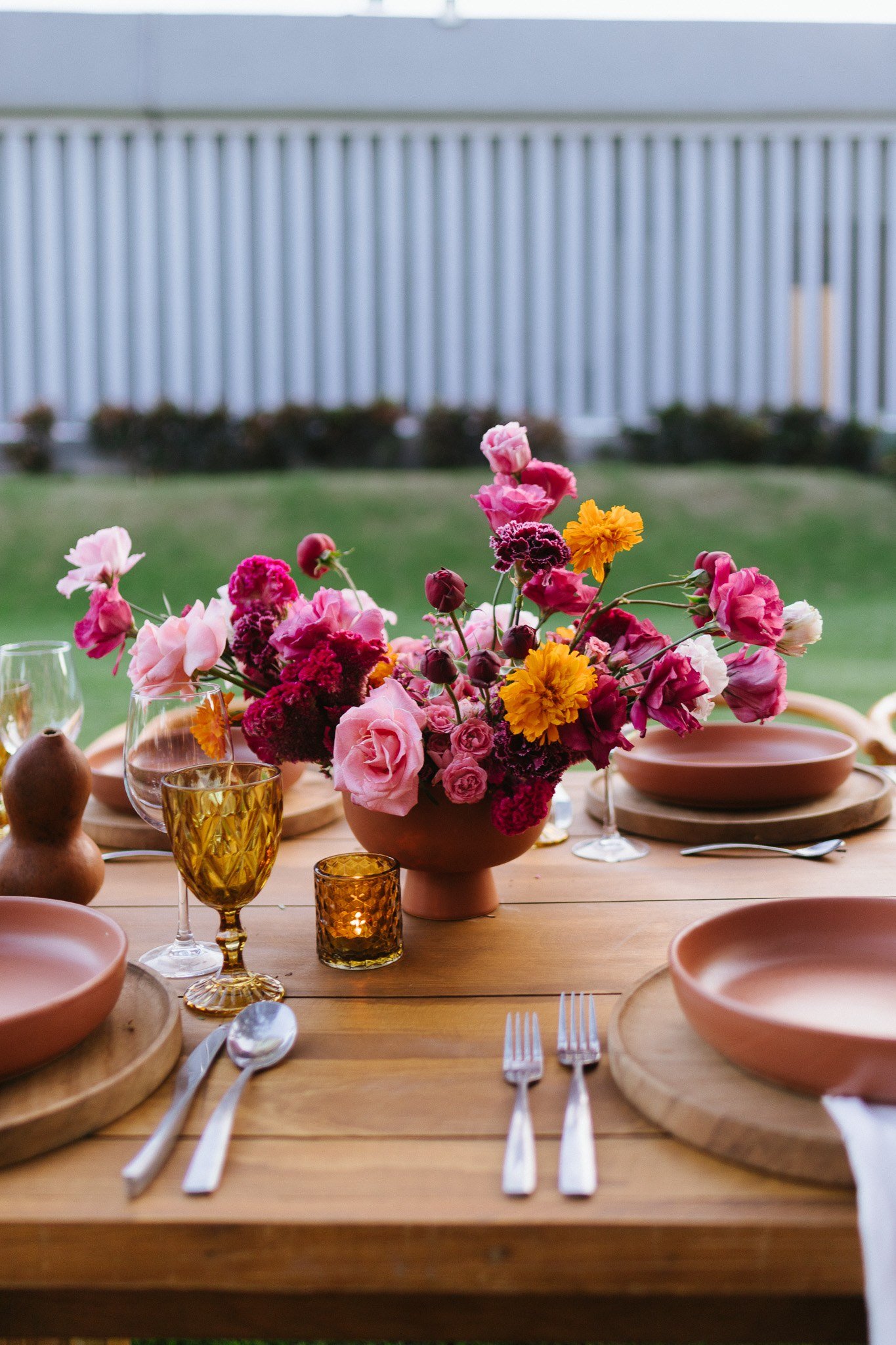 Place setting with a terracotta plate, clay gourd and a low magenta arrangement