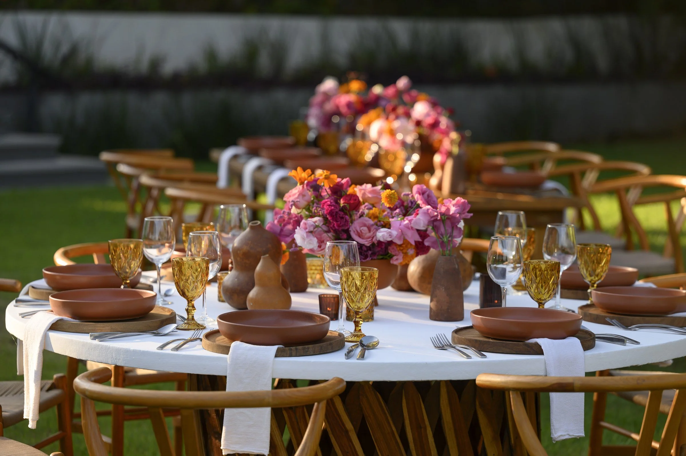 Round table with terracotta plates, amber glassware and a magenta centerpiece