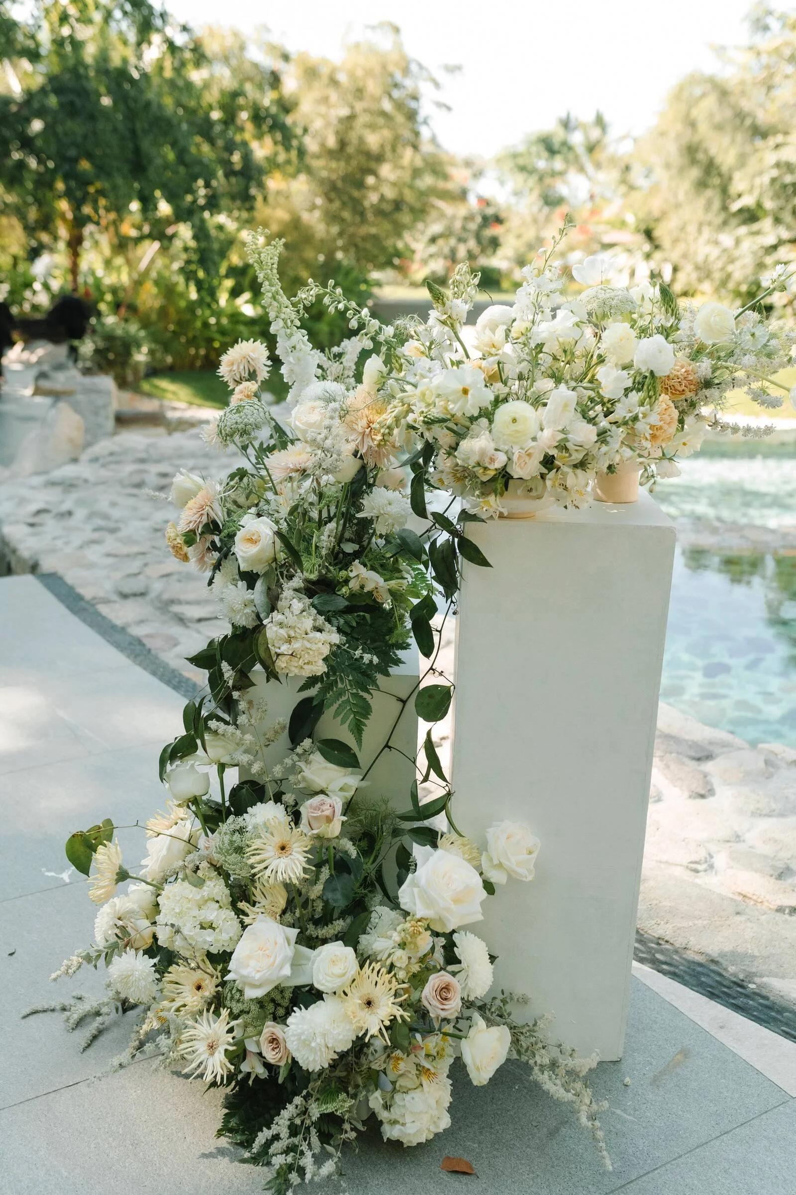Grounded arrangement of mums, roses and Queen Anne's lace spilling off a pedestal at Garza Blanca