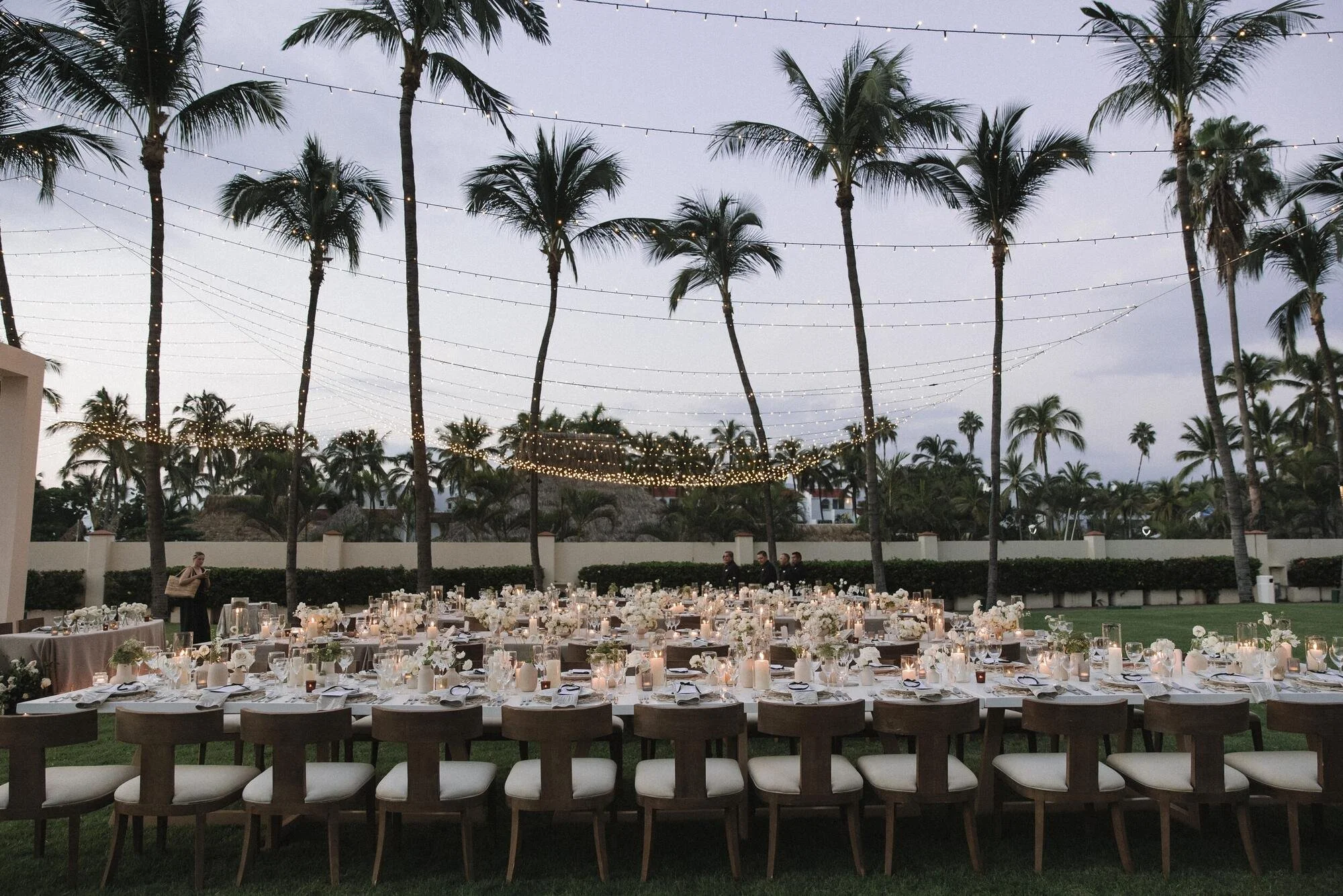 Reception long tables under palms and string lights at Grand Velas
