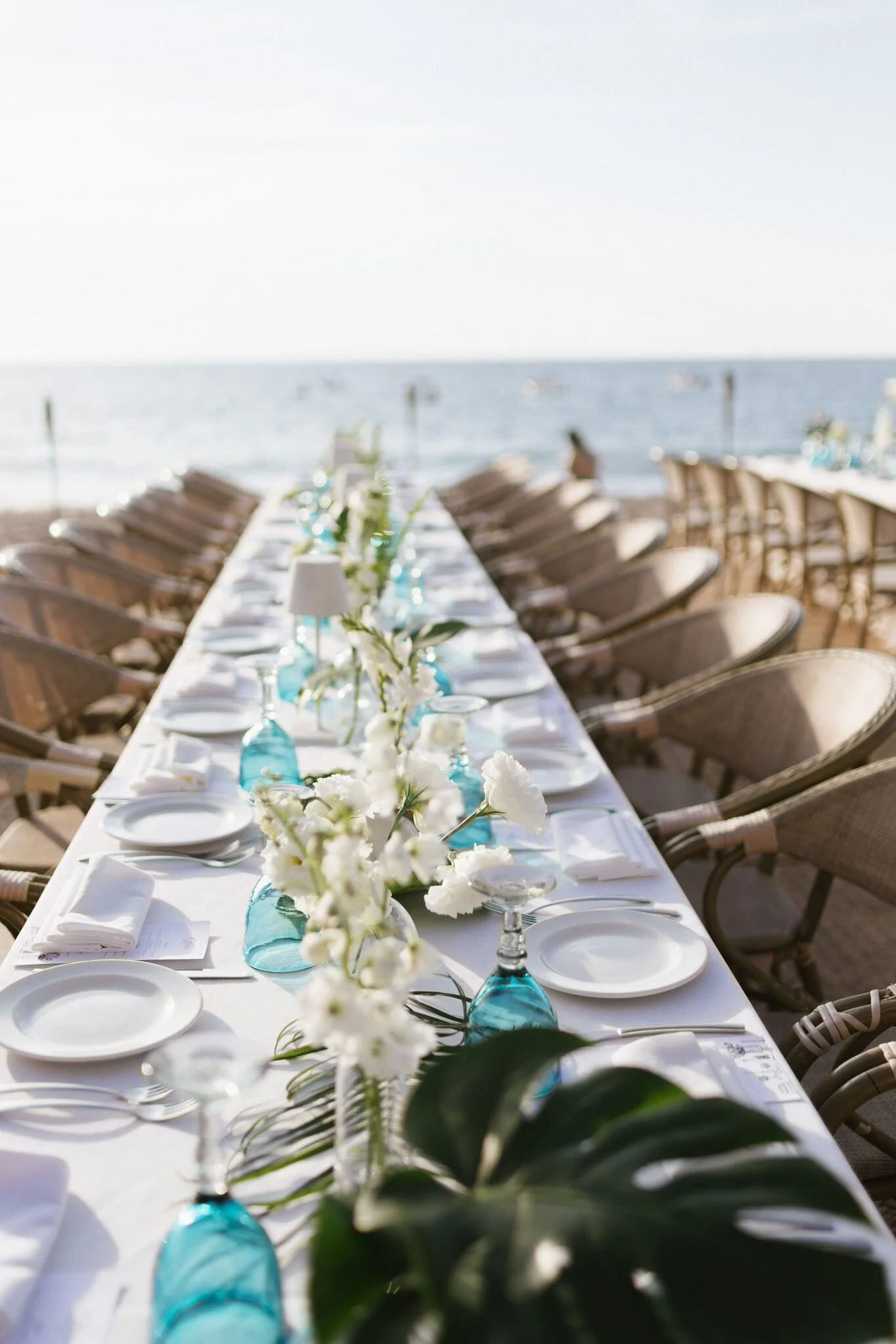 Long table with white bud vases and turquoise glassware at a welcome party at El Dorado