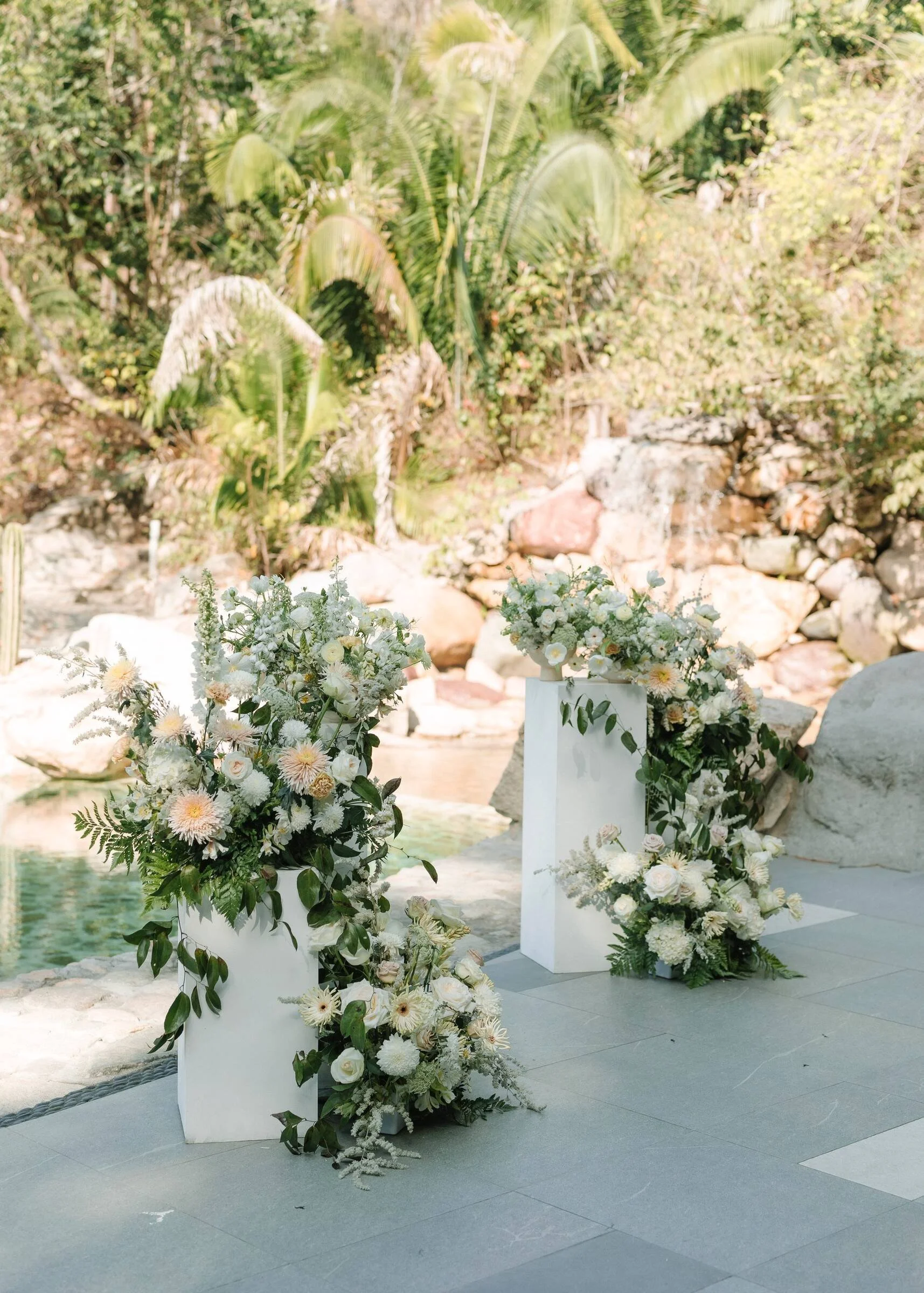 Two white pedestals with grounded white florals beside the pool at Garza Blanca, Puerto Vallarta