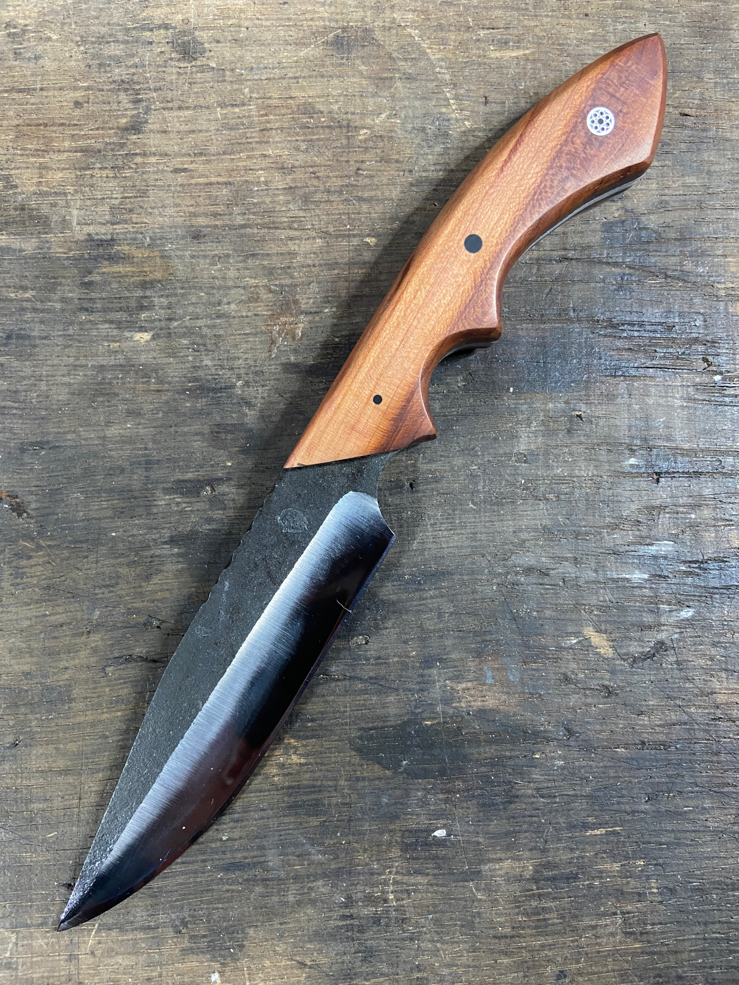 Couteau droit forgé brut de forge avec un manche en bois brun sur fond de bois de chêne.