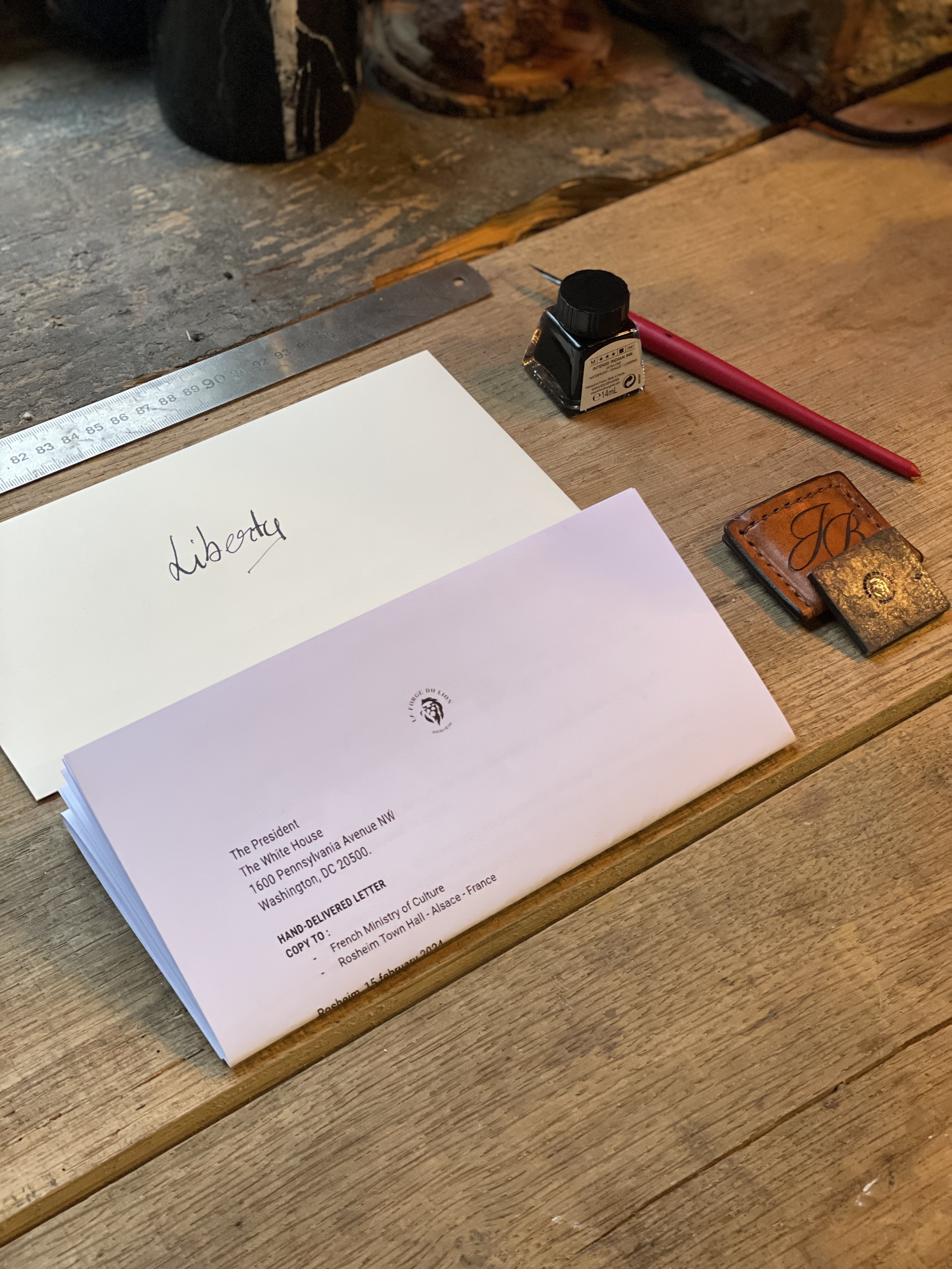 Une lettre blanche avec son enveloppe et un bout d'acier sur une pochette en cuir orange sur fond de bois clair et foncé.