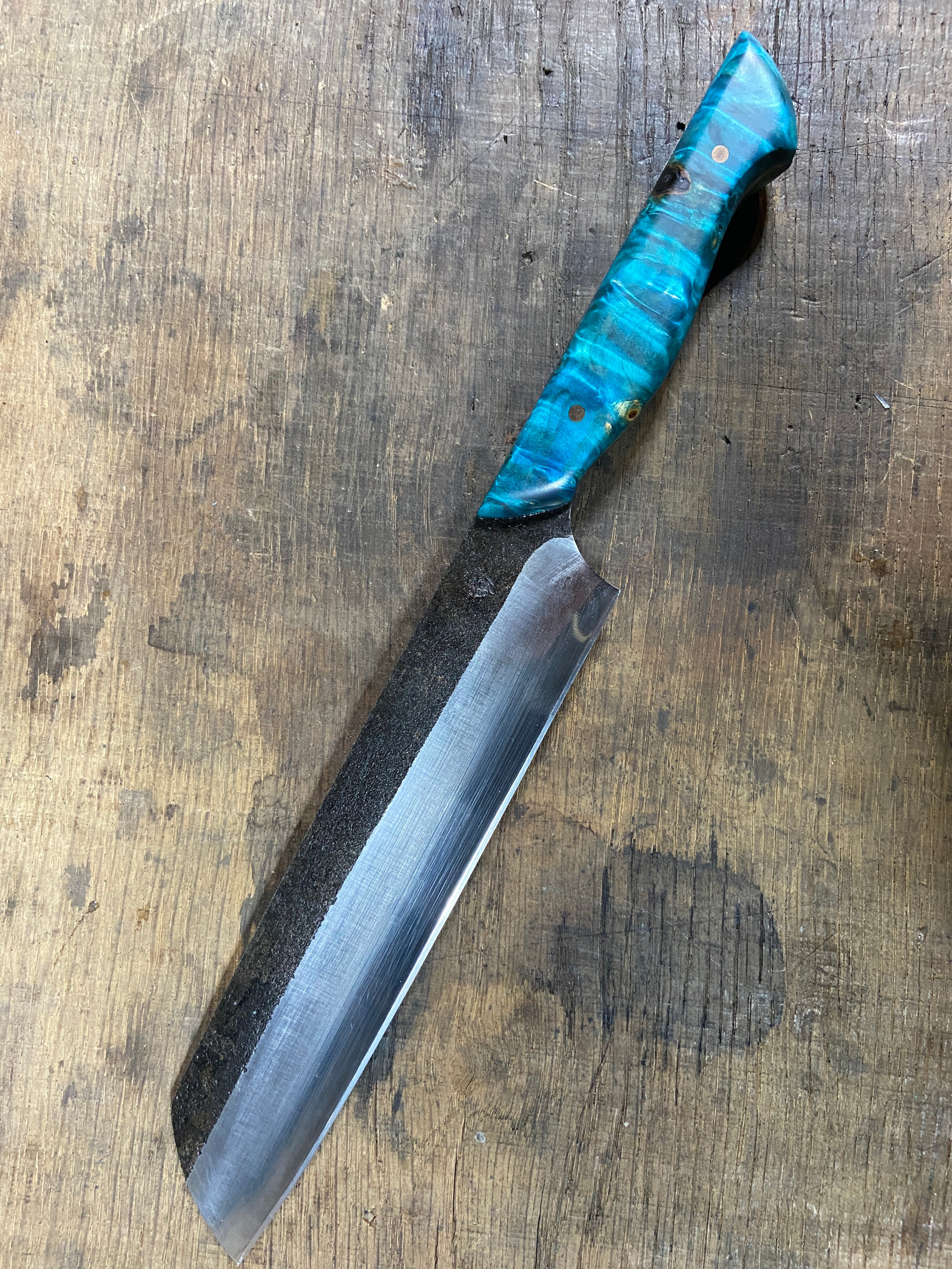 Couteau de Chef forgé brut de forge avec un manche en bois bleu sur fond de bois de chêne.
