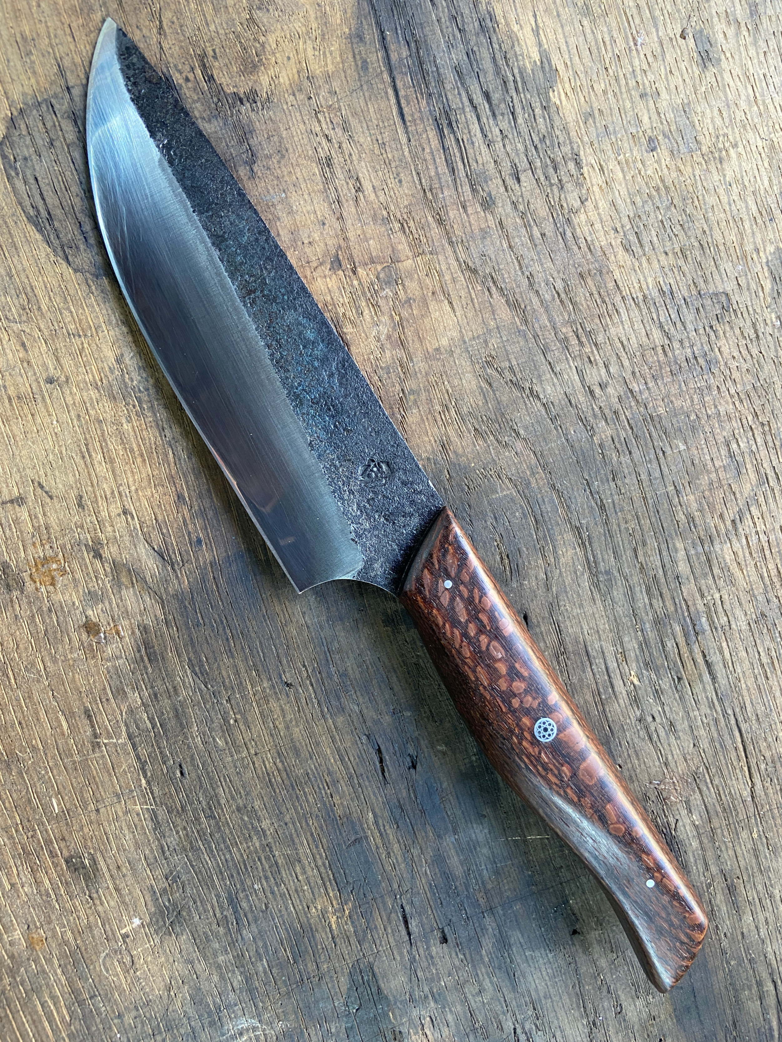 Couteau de Chef forgé brut de forge avec manche en bois marron sur fond de bois de chêne.