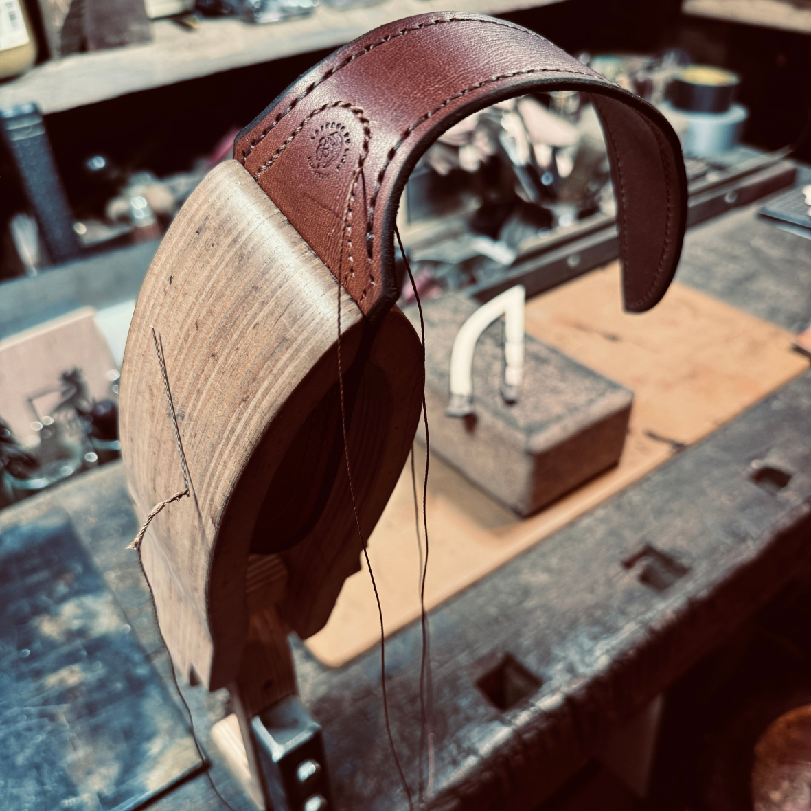 Du cuir avec une aiguille et du fil dans un chevalet fixé sur un établi en bois clair et foncé