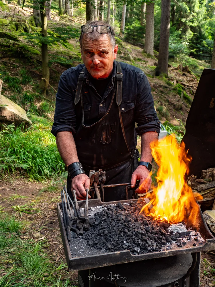 Portrait de Michel Reibel devant sa forge en plein air, en forêt