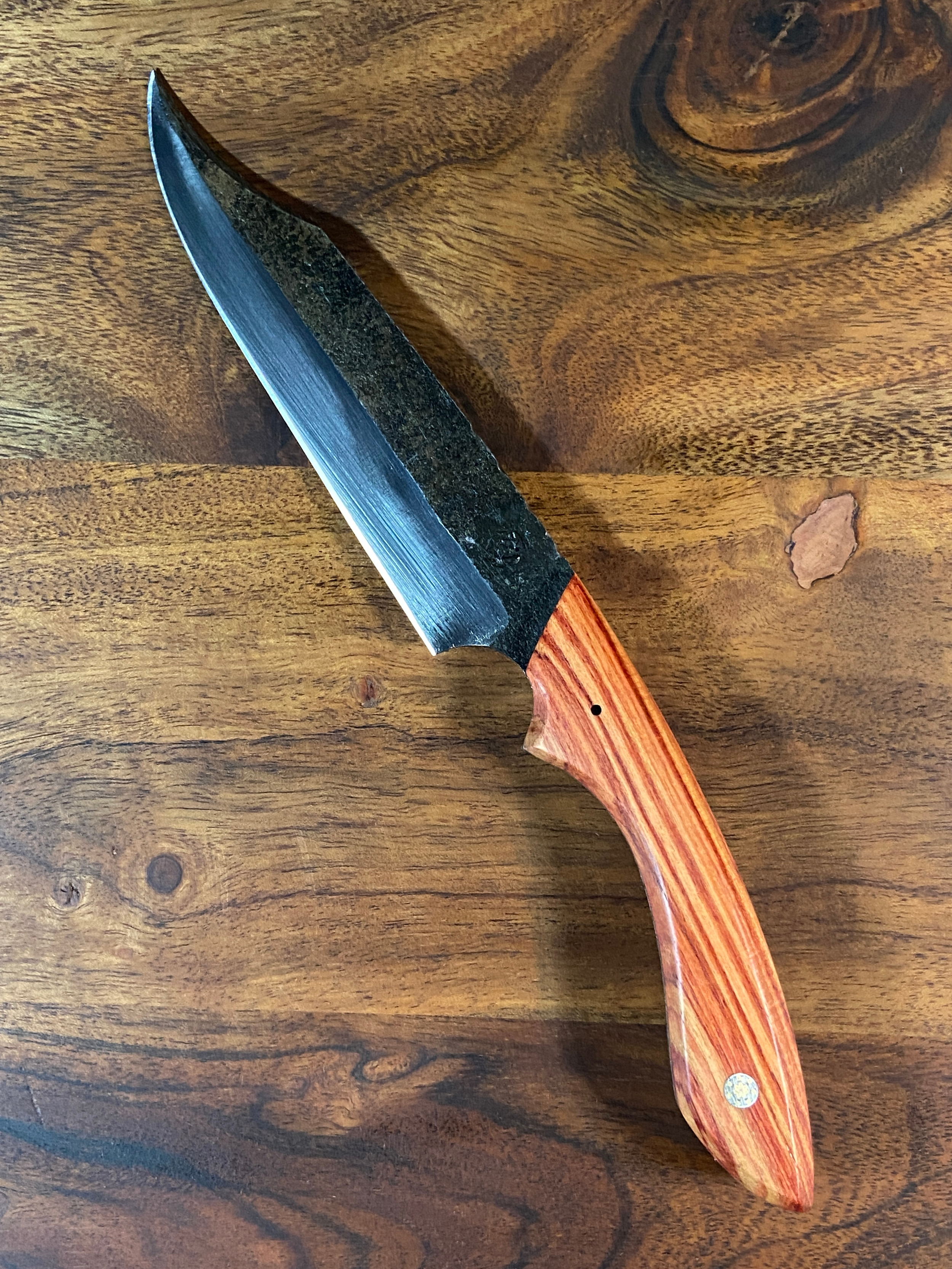 Couteau forgé brut de forge avec manche en bois rouge et blanc sur fond de bois marron.