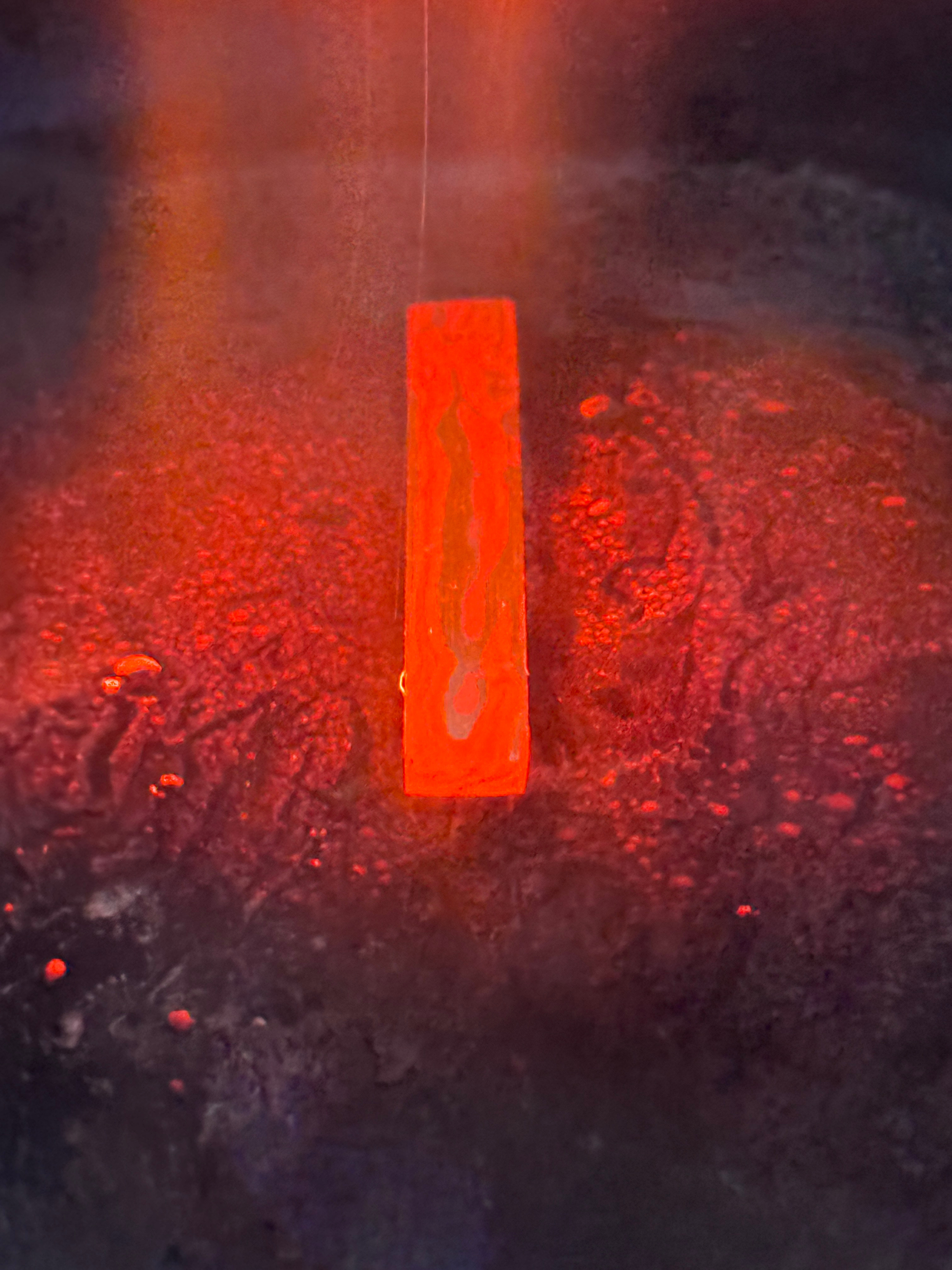Une flamme rouge-orange dans une surface sombre, évoquant un feu ou une matière en combustion, avec des étincelles et des cendres autour.