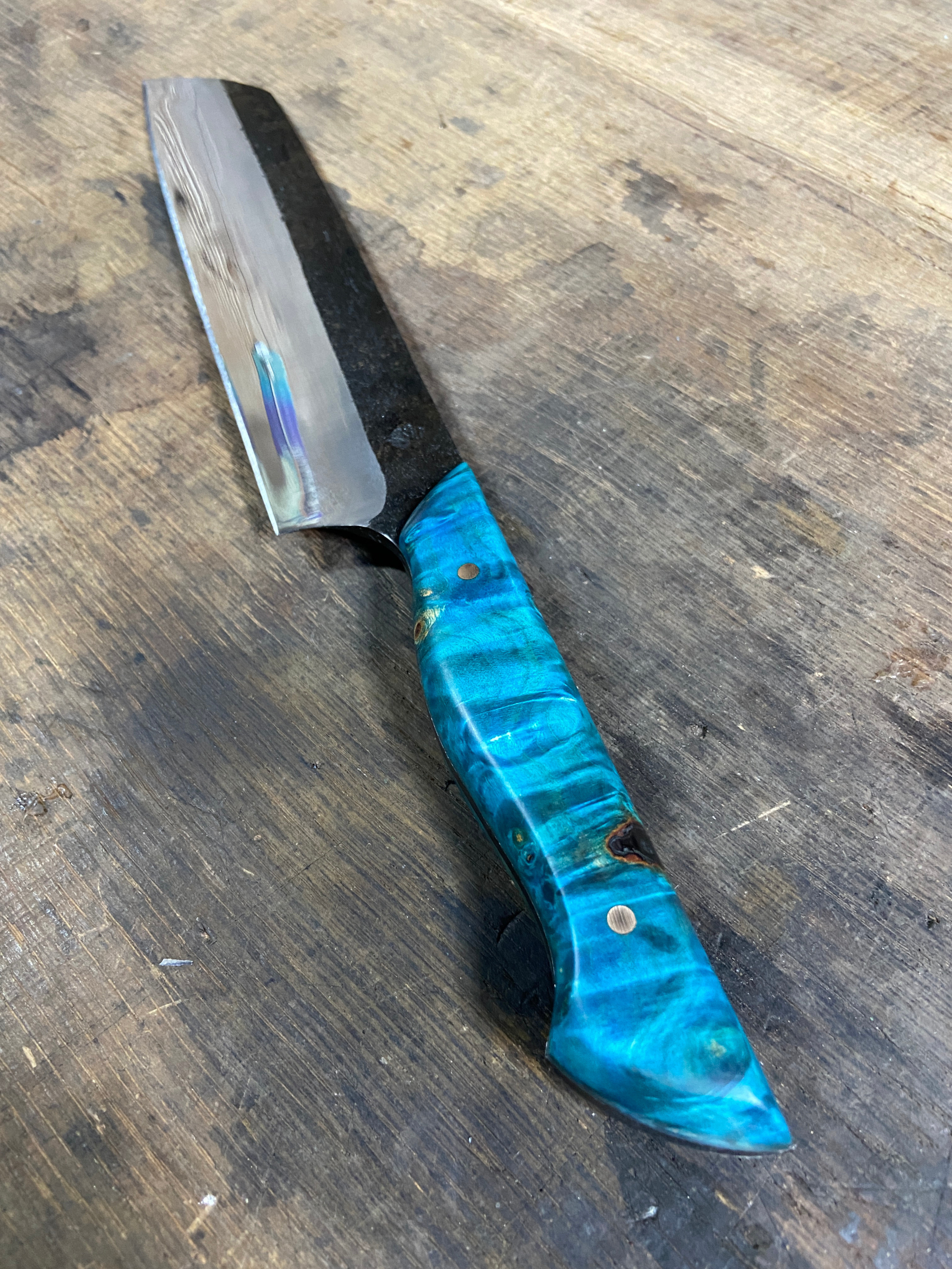 Couteau de Chef forgé brut de forge avec un manche en bois bleu sur fond de bois de chêne.