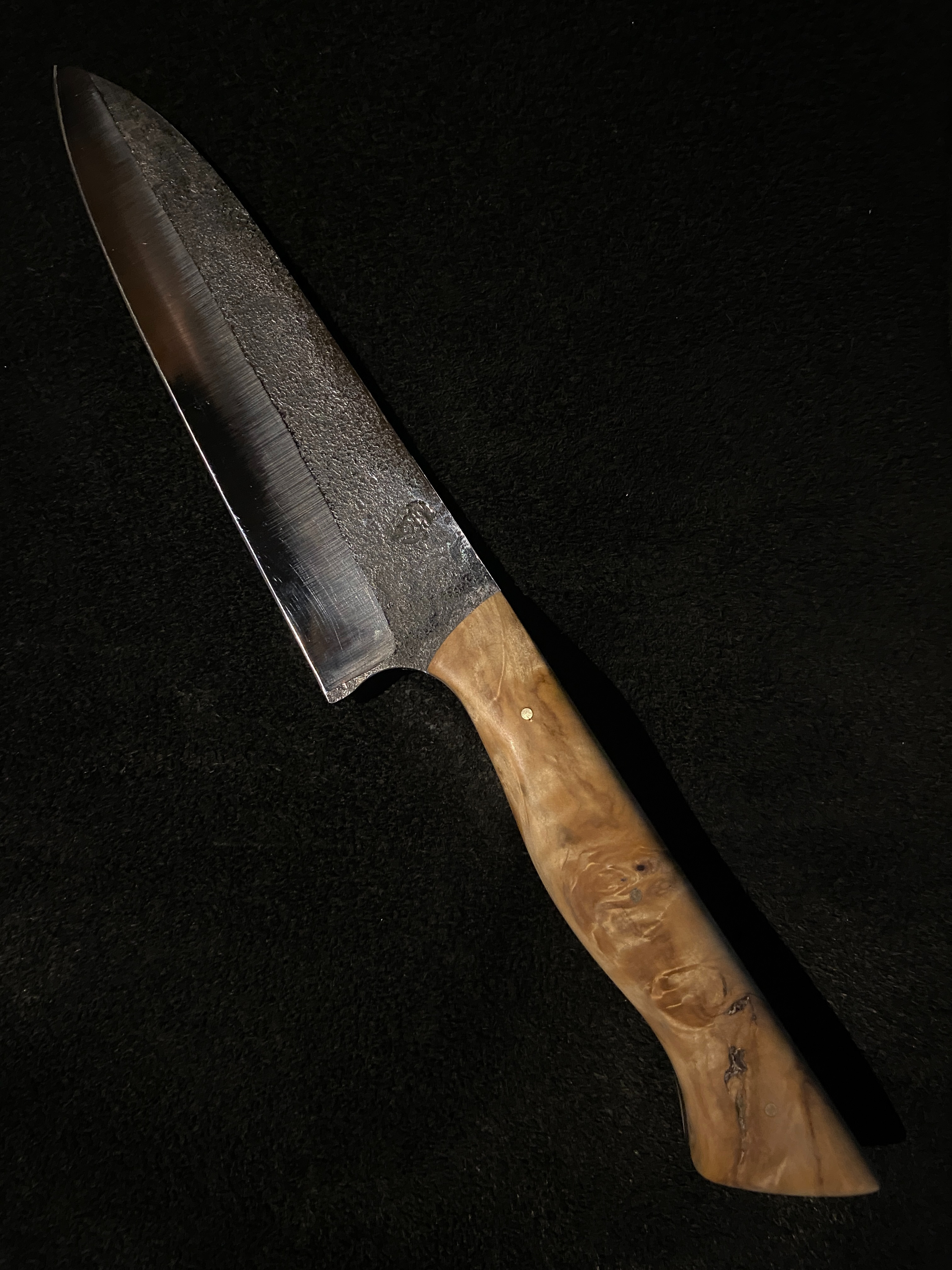 Couteau droit de cuisine forgé brut de forge et manche en bois marron sur fond noir.