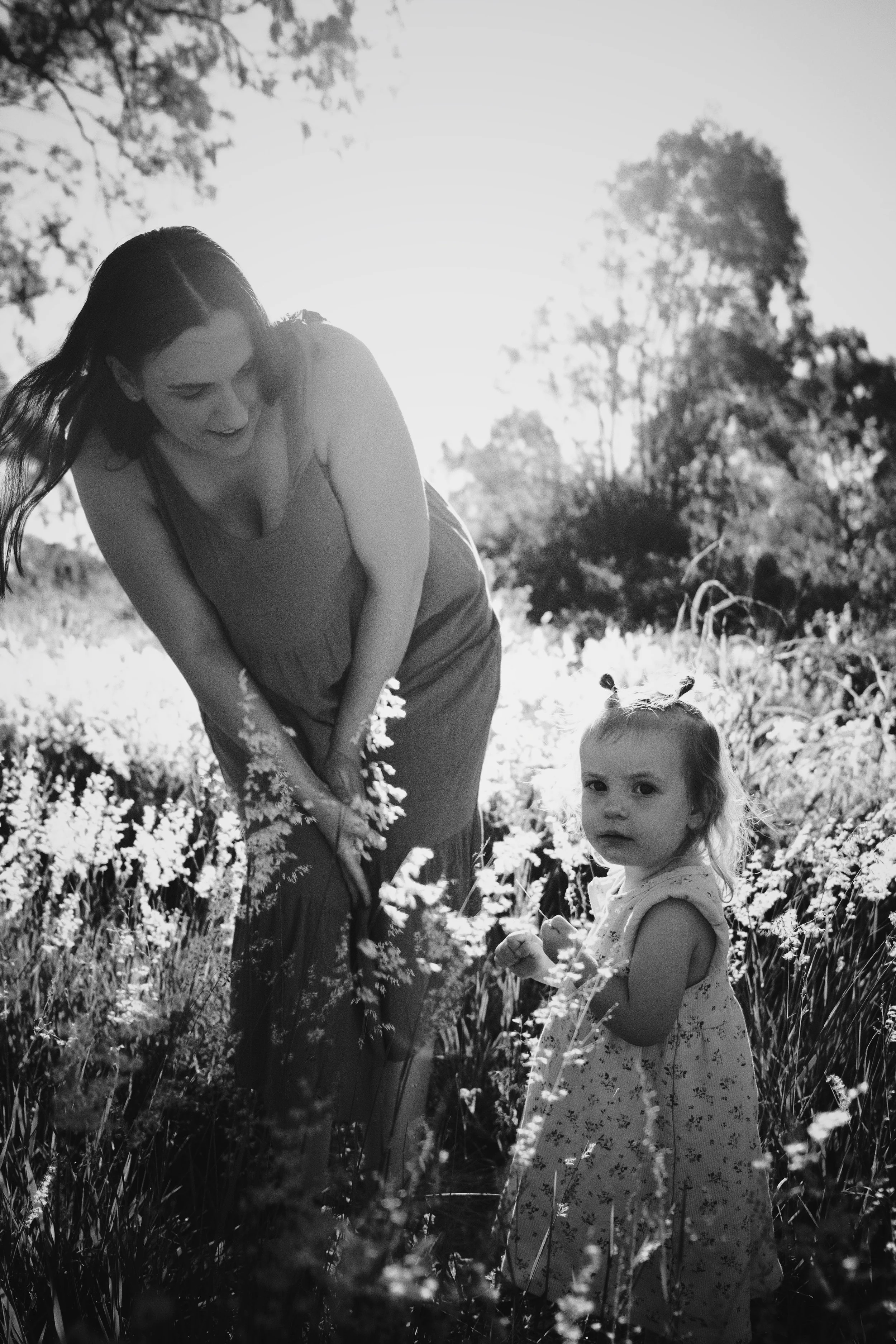 A woman and a young girl in a field of flowers, with sunlight behind them, captured in black and white.