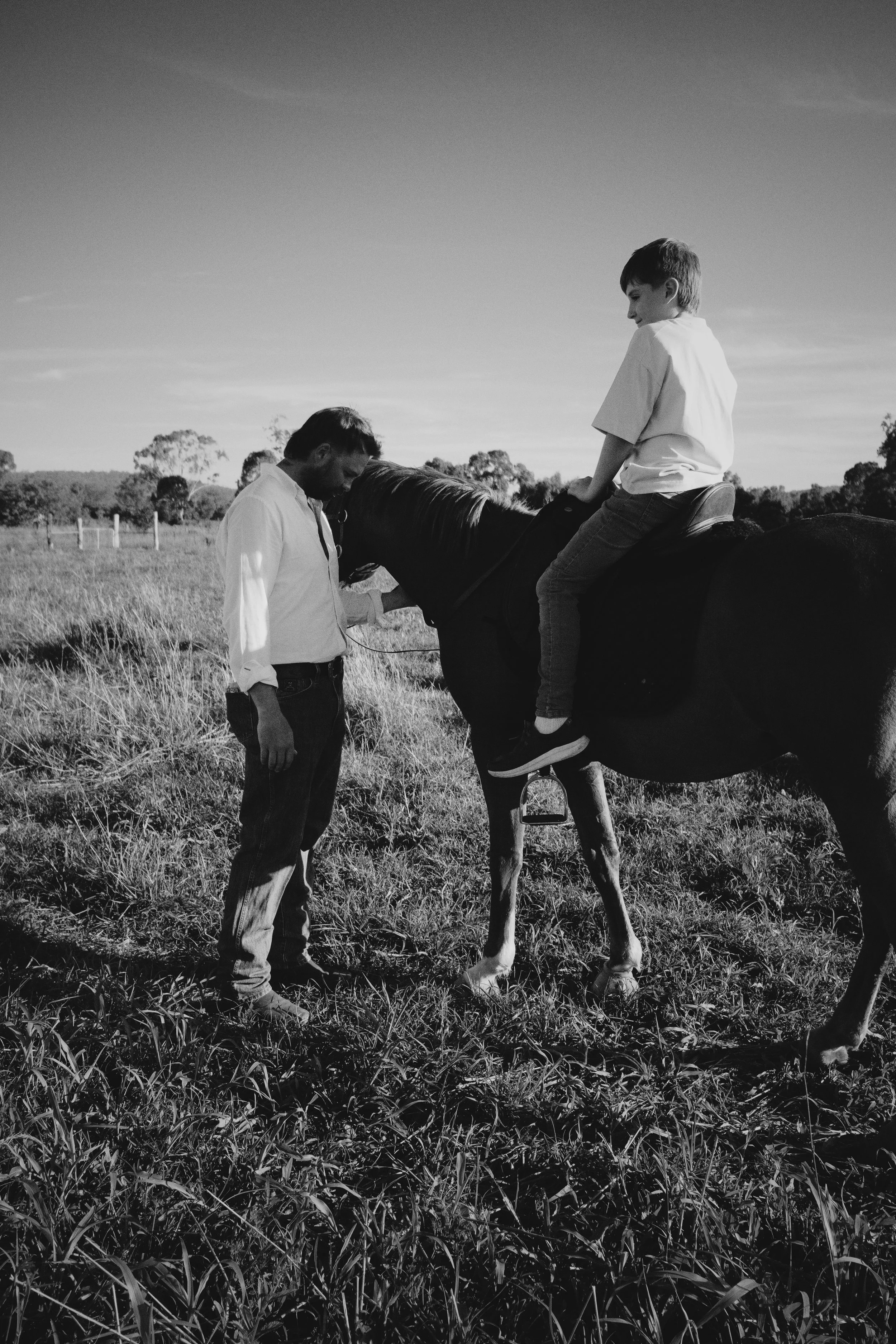 A child sitting on a horse being held by an adult man in a grassy field.
