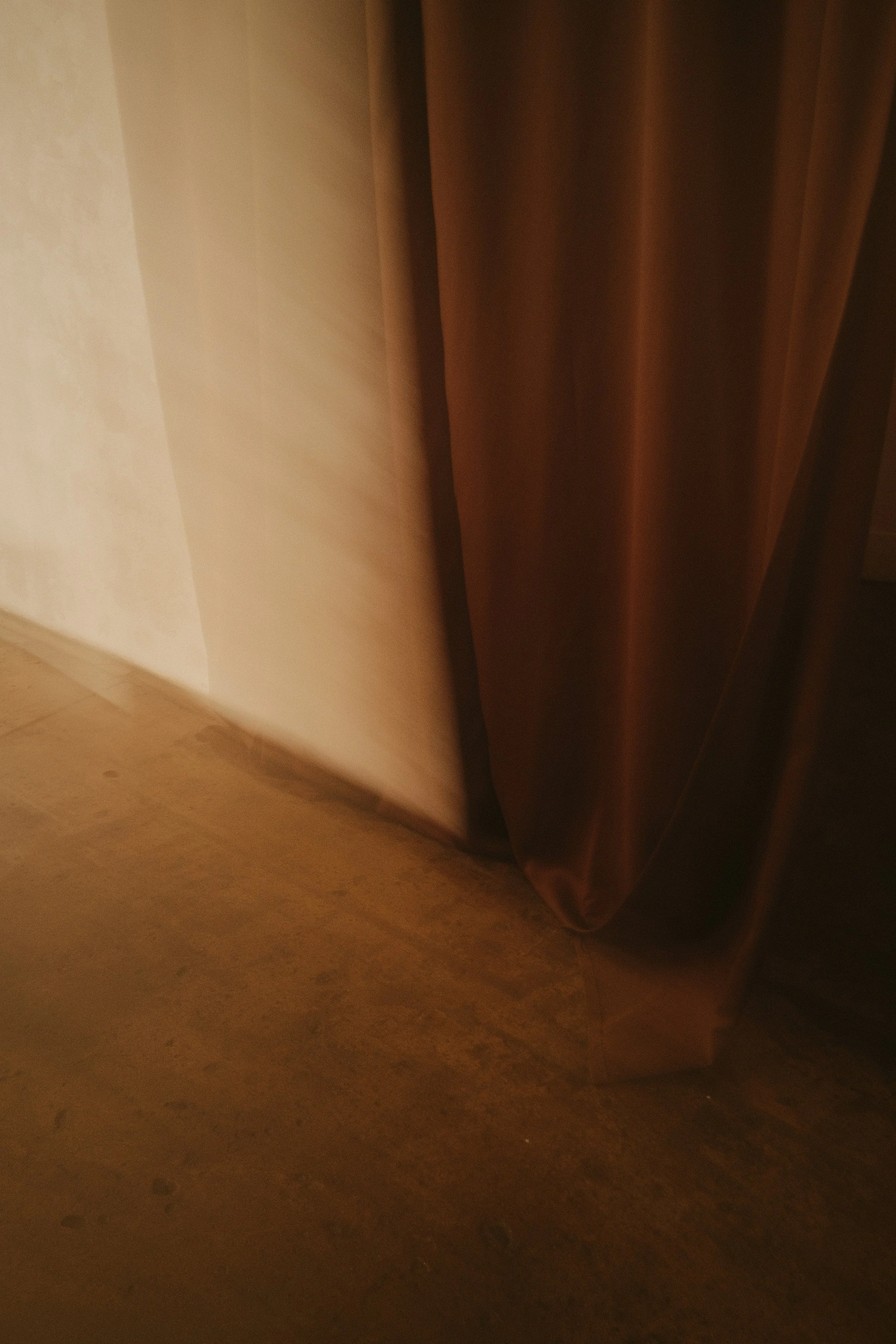 Close-up of a brown curtain draped near a cream-colored wall and wooden floor.