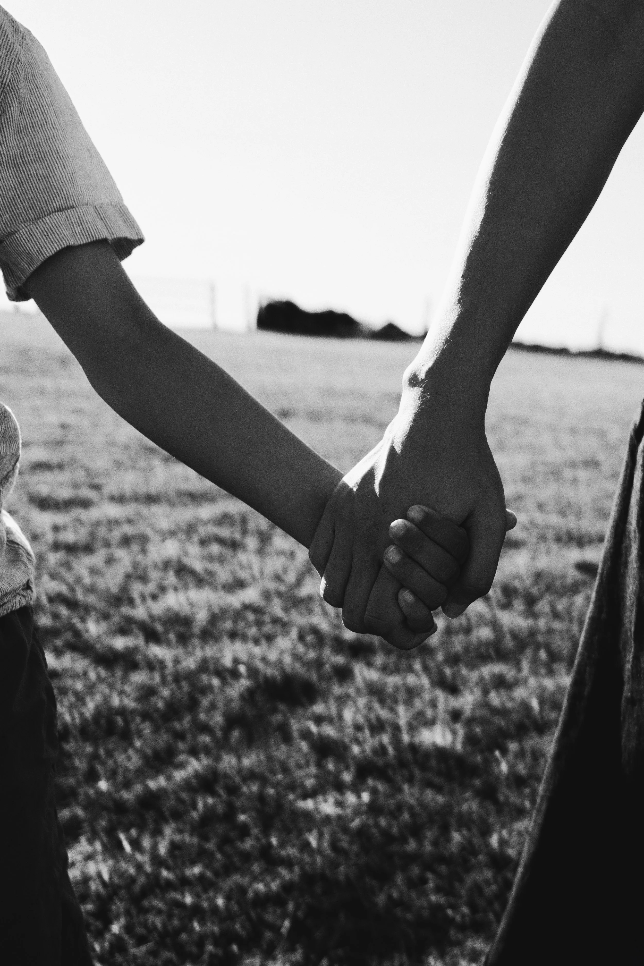 Two people holding hands outdoors on a grassy field, black and white photograph.