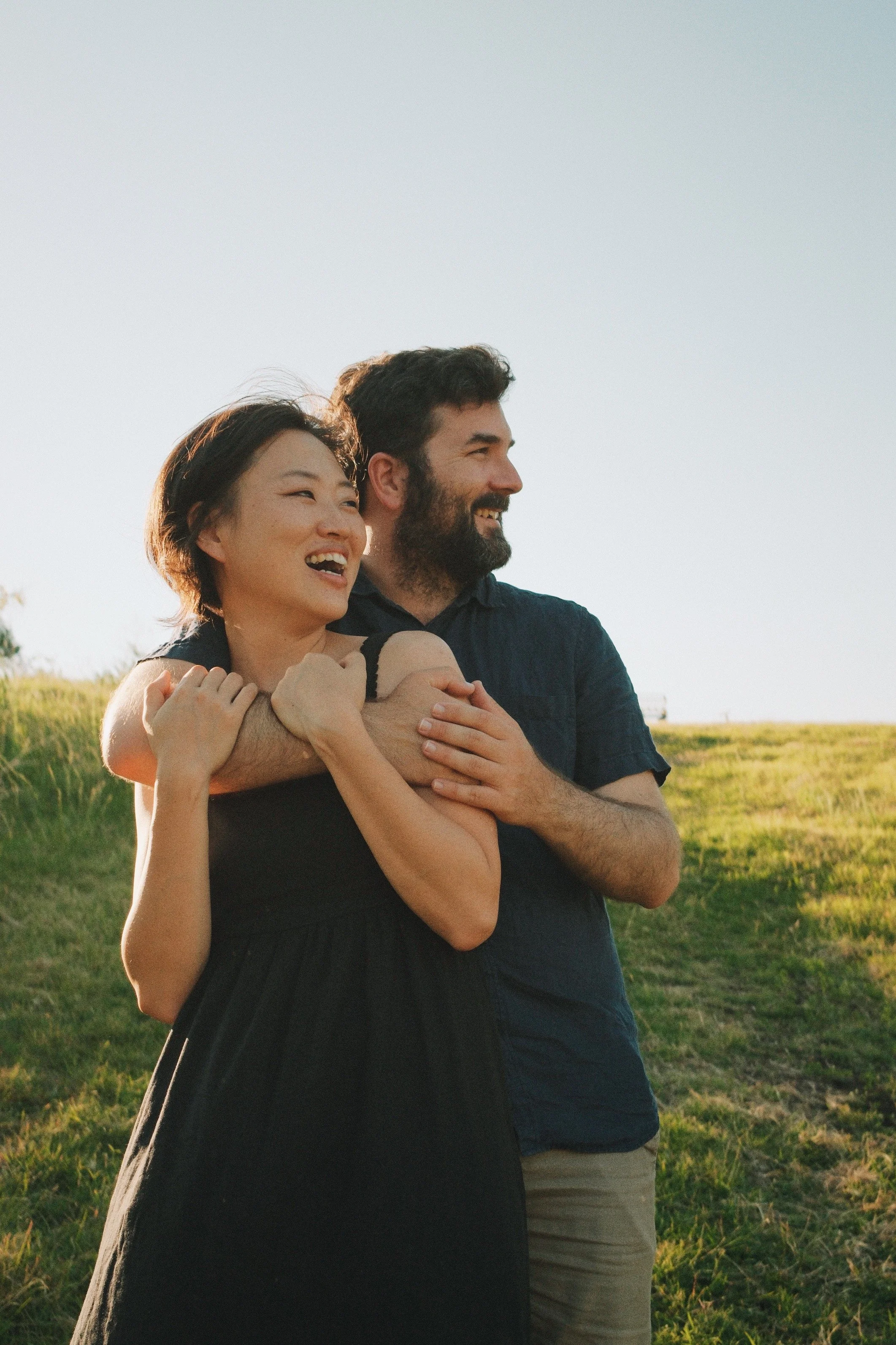 A happy couple embracing outdoors during sunset, with a grassy field in the background.