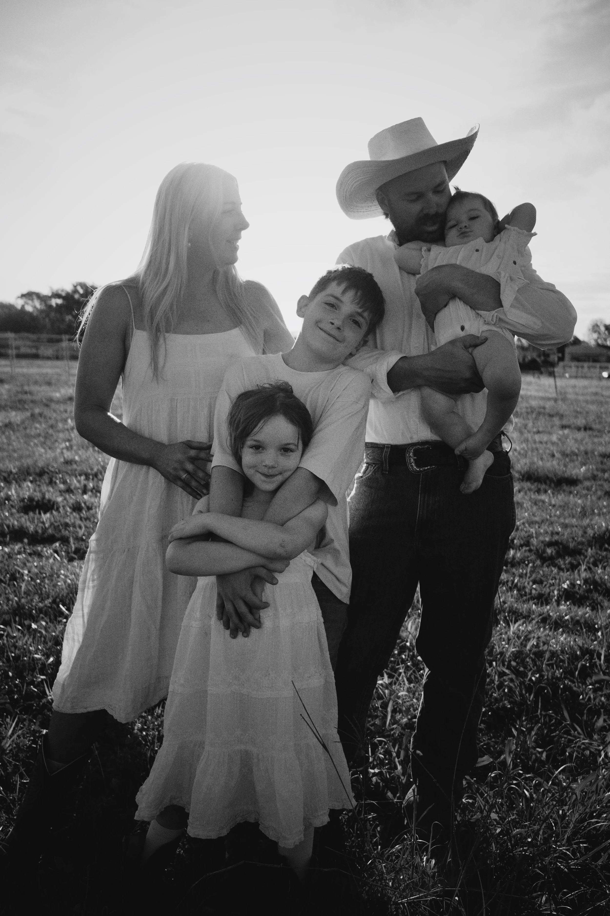 A family of five outdoors, a woman and a man with three children, standing in a grassy field during sunset.