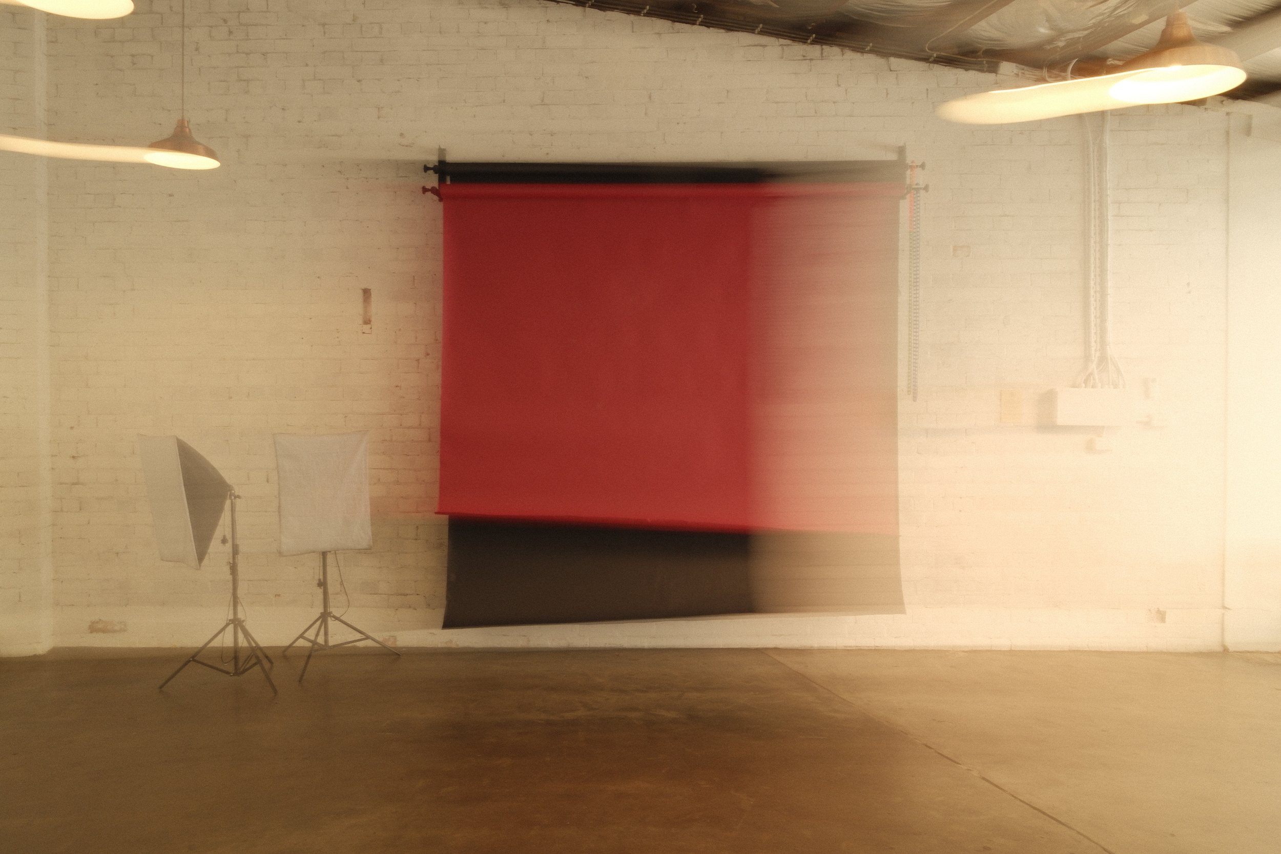 Photography studio with a red and black backdrop, two photography lights with umbrellas, and a white brick wall.