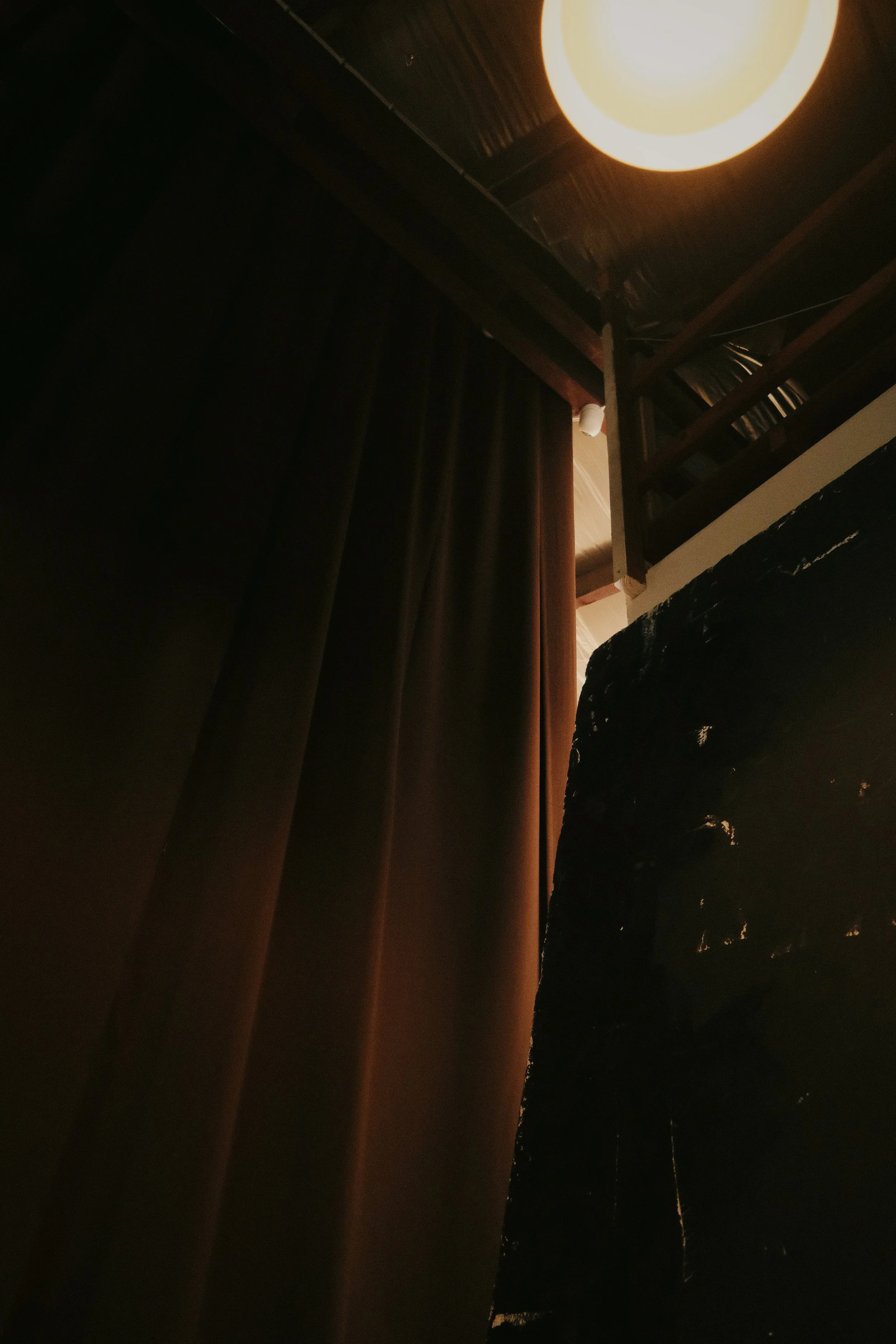 Lighting fixture illuminating a dark space with curtains and a wooden balcony visible.