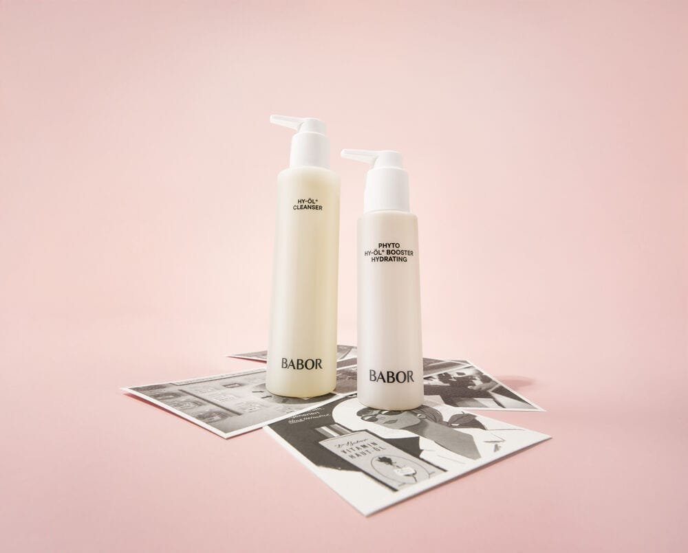 Two skin care bottles with pumps labeled 'BABOR' on top of grayscale posters, on a pink gradient background