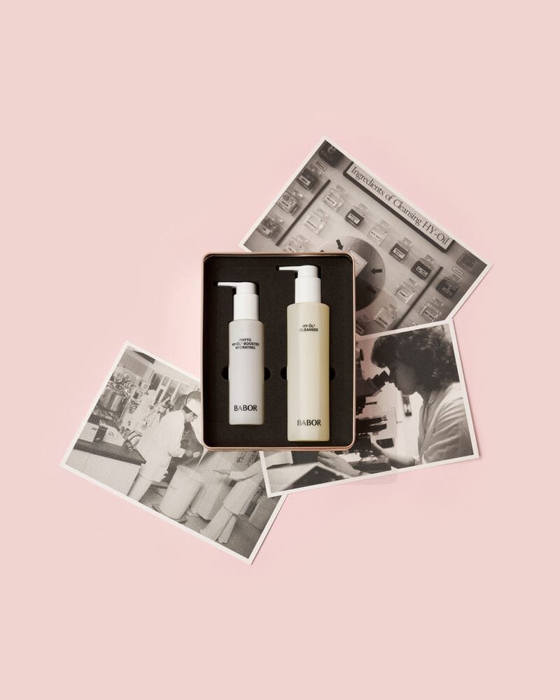 opened box with 2 BABOR bottles embedded in dark foam material, grayscale posters behind on a pink gradient background