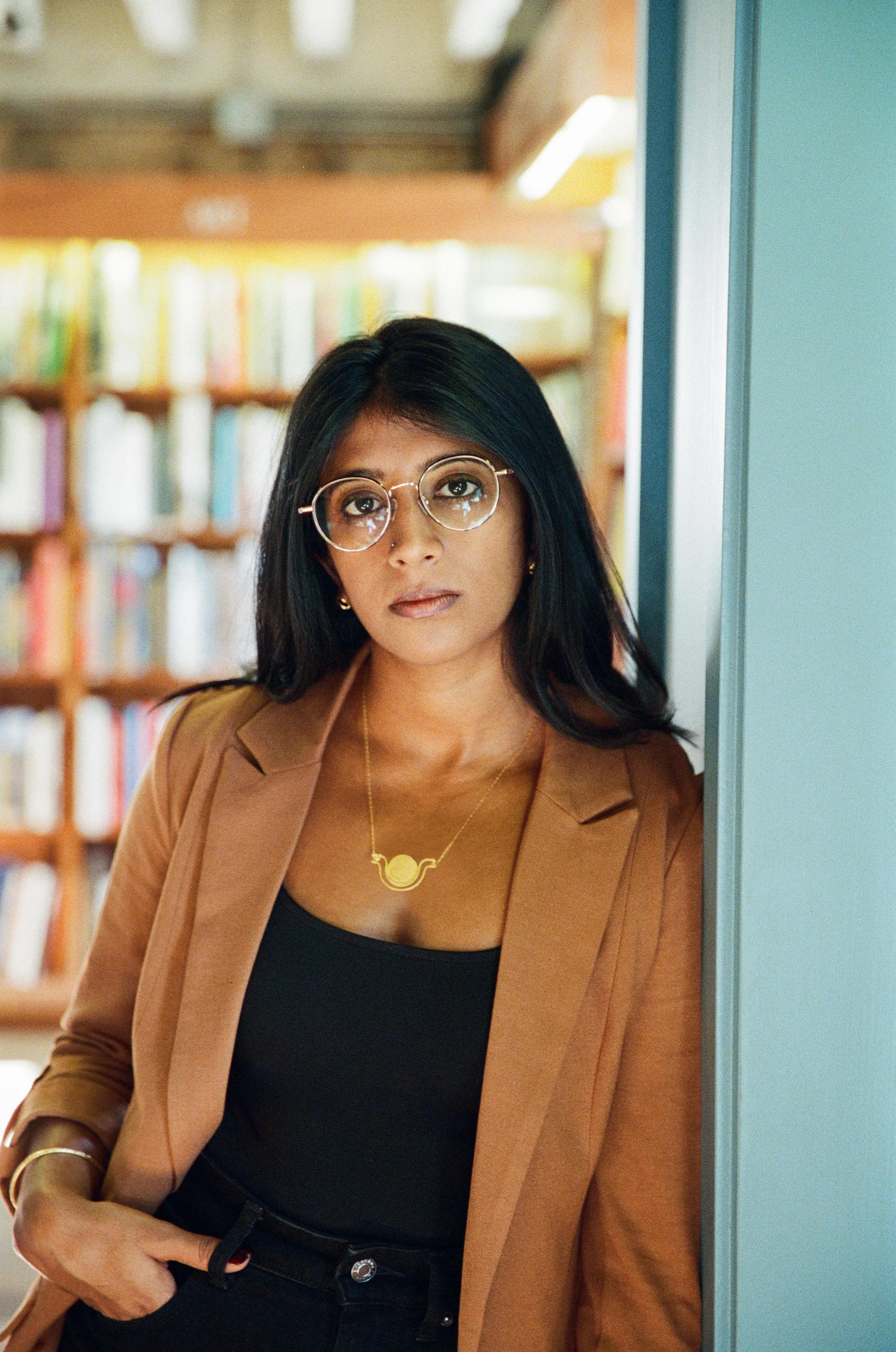 Sanjena Sathian standing in front of a brown bookshelf.