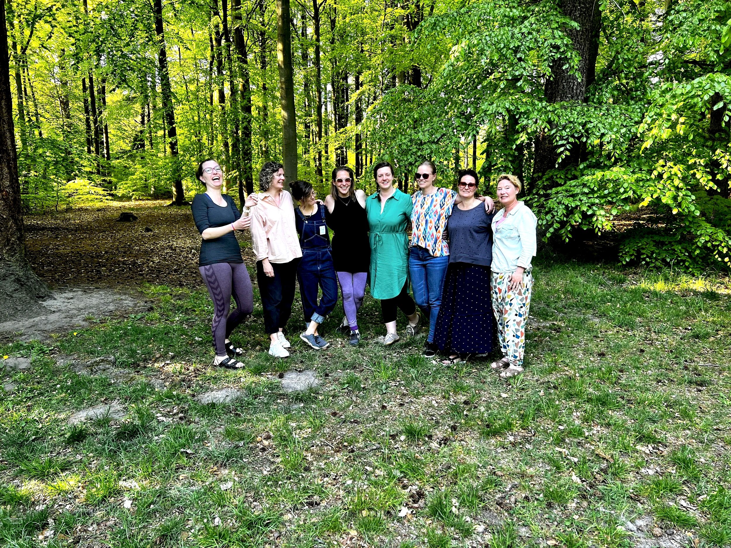 En gruppe kvinder står sammen i en skov, smilende og poserende for kameraet.