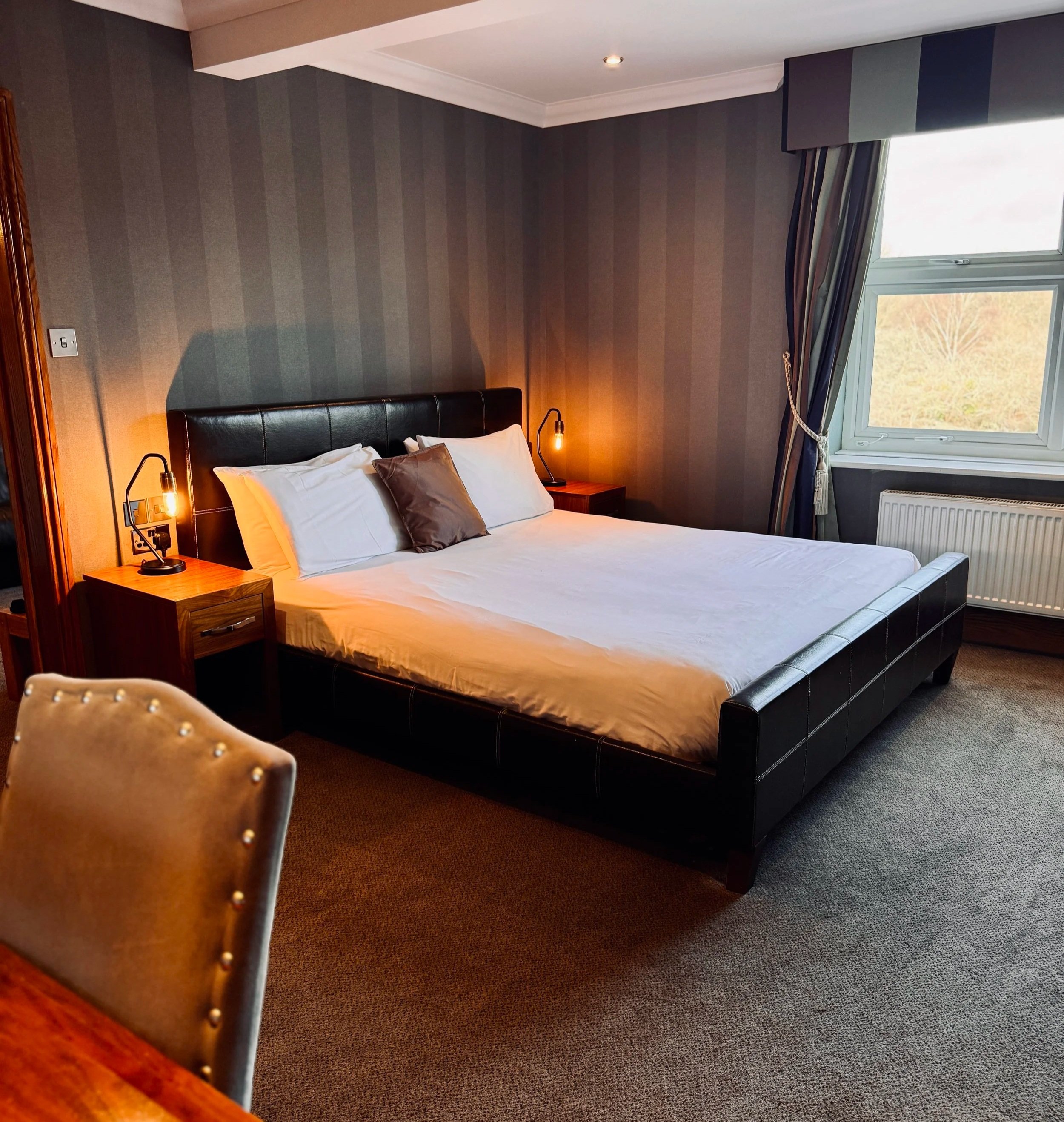 A bedroom with a large 5ft bed, nightstands, lamps, and a window showing a landscape outside.