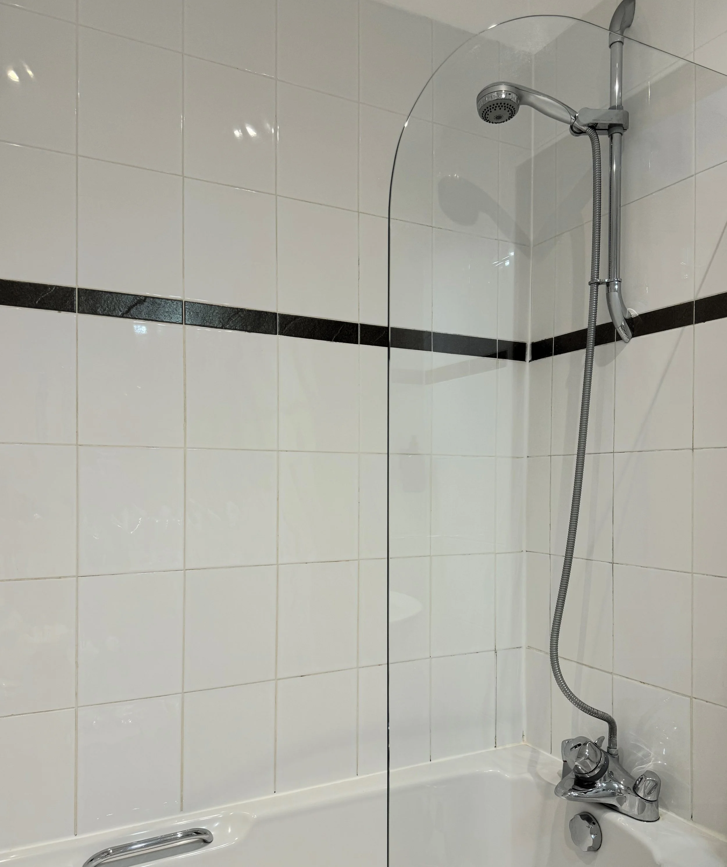 A shower area with a glass splash guard, a handheld showerhead, and tiled walls.