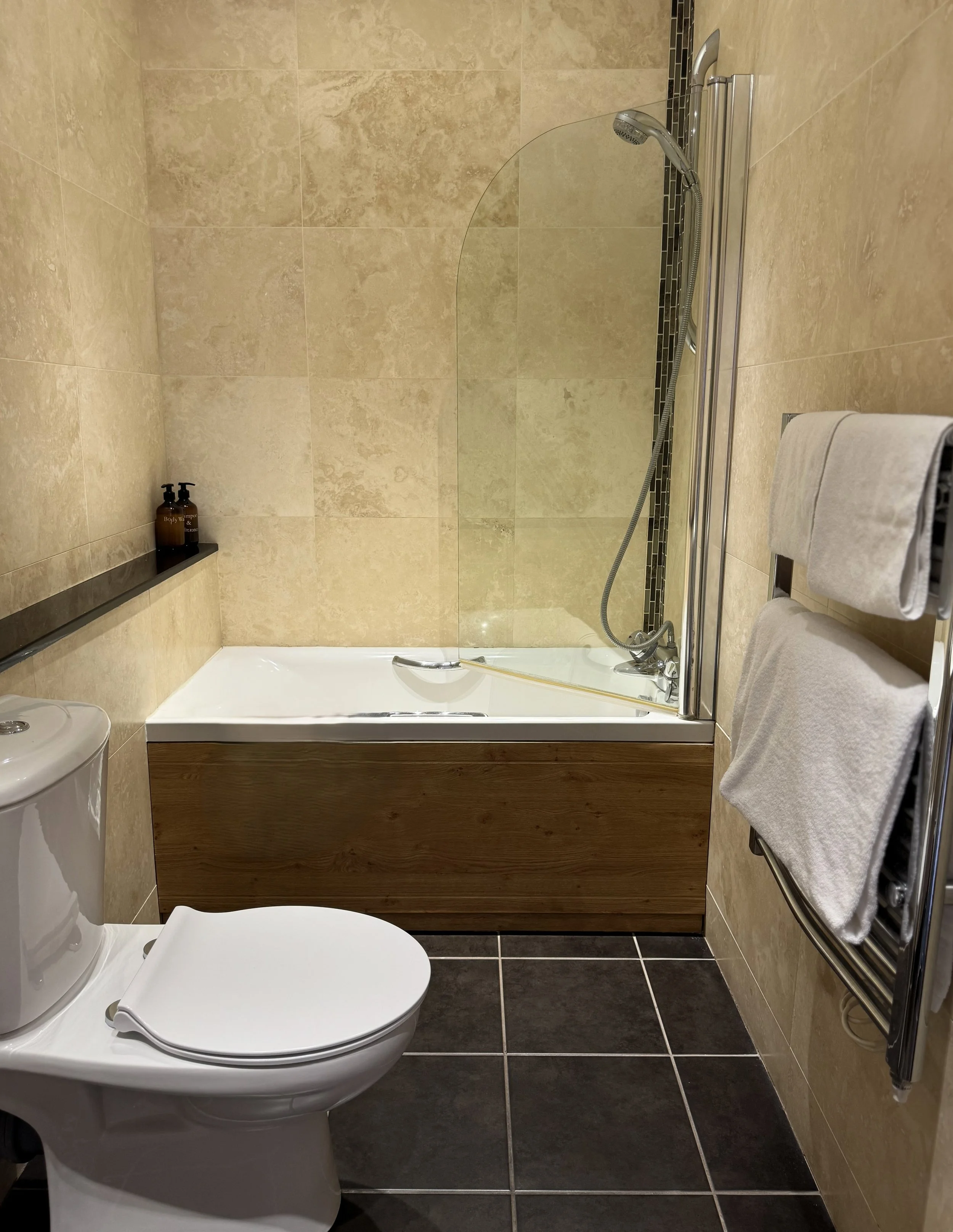 A bathroom with a toilet, bathtub with a glass partition, and towel rack.