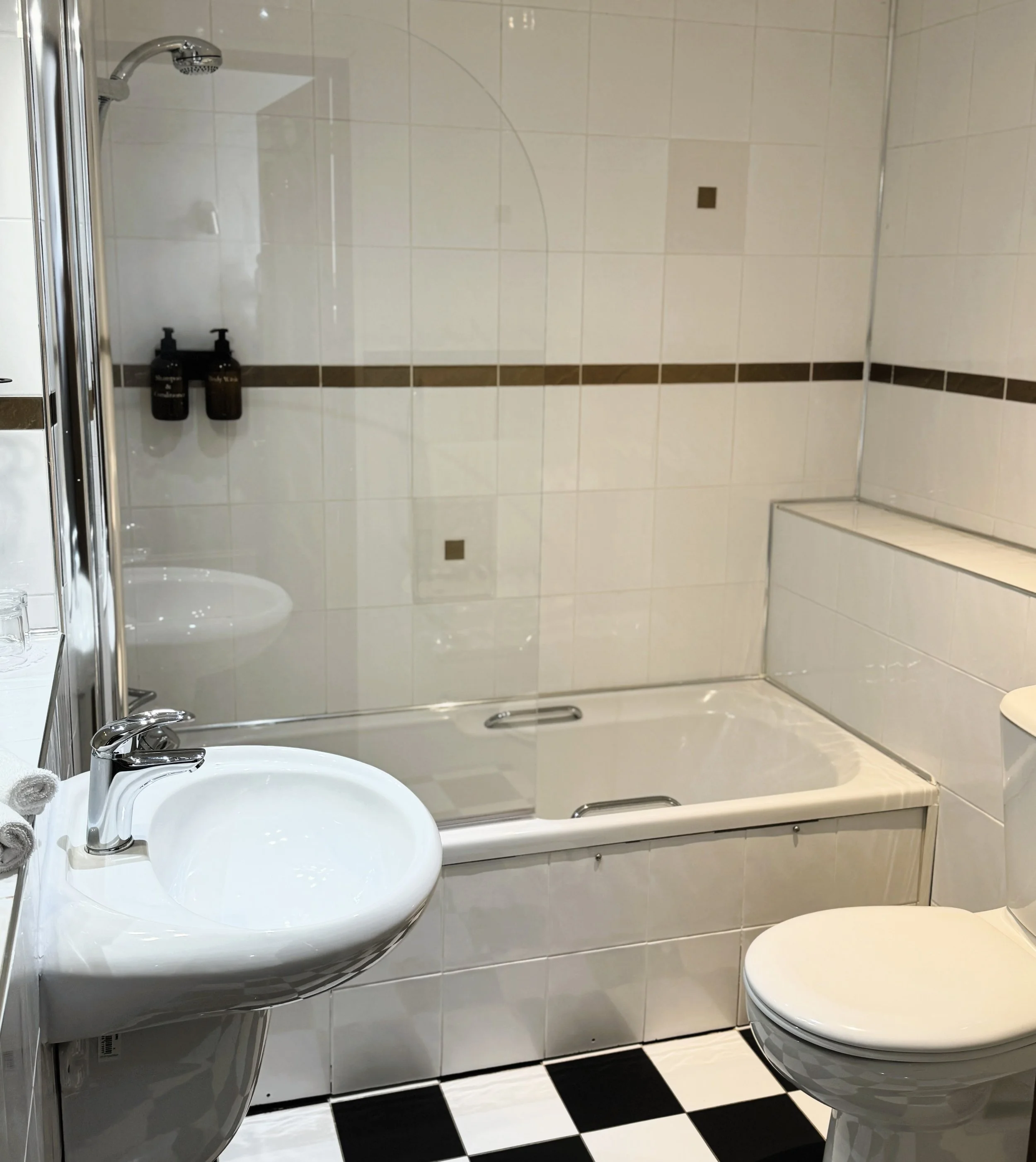 Bathroom with a sink, a bathtub with a glass shower door, a toilet, and tiled walls with a horizontal brown stripe.