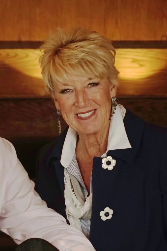 Smiling woman with short blonde hair wearing a floral shirt, indoors.
