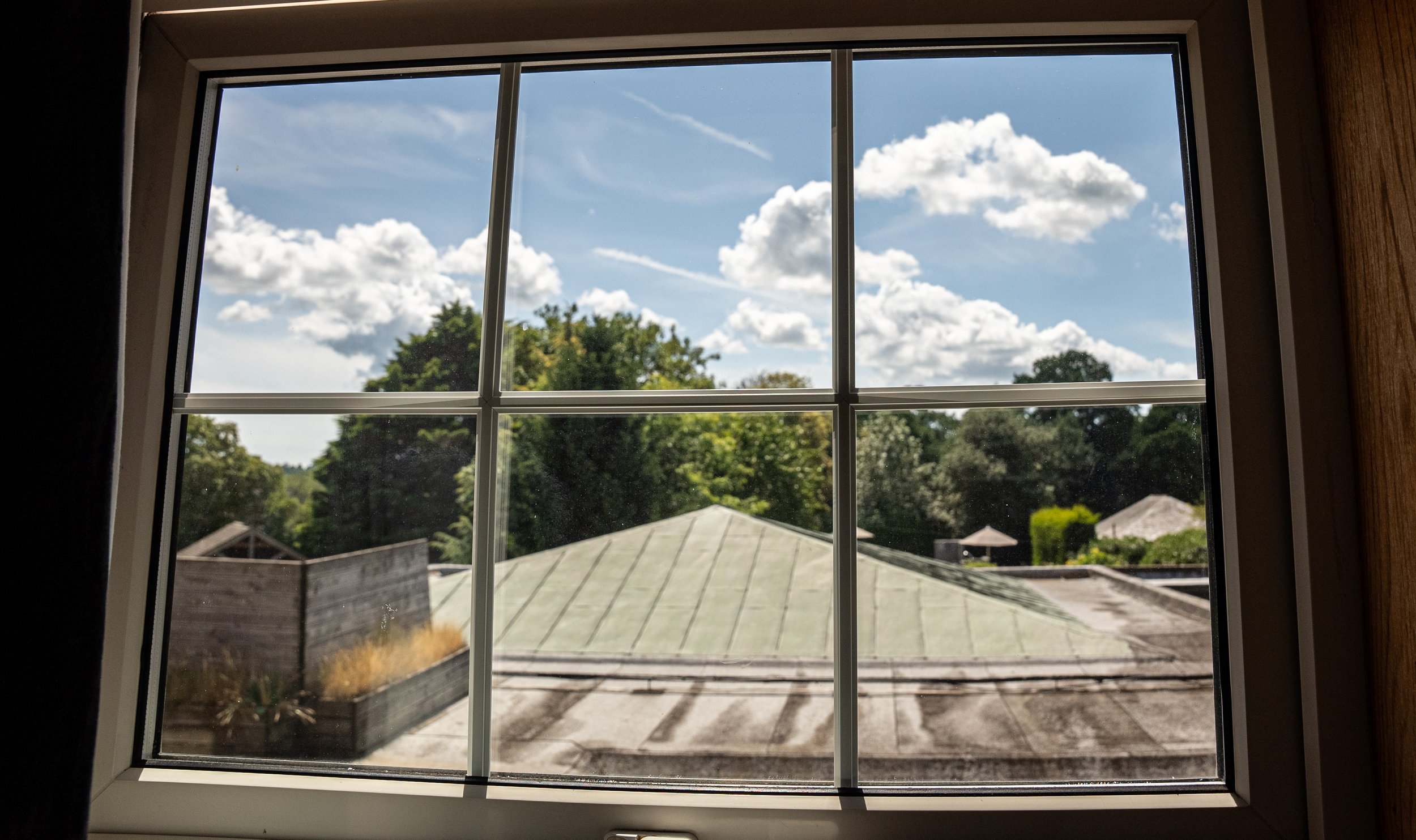 View through a window showing a rooftop, trees, and a partly cloudy sky.