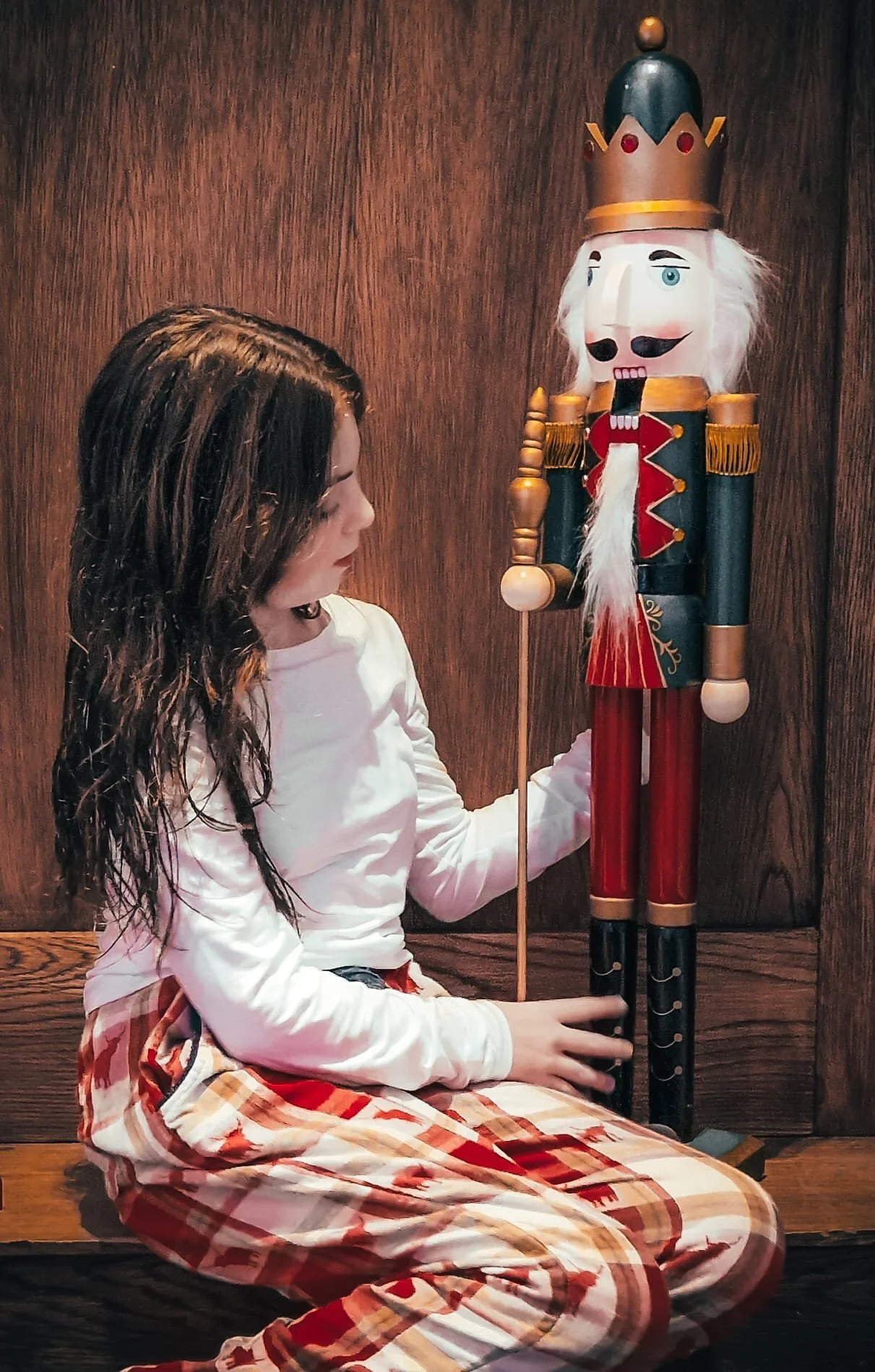 A young girl sitting on a wooden bench holding a large toy nutcracker soldier.