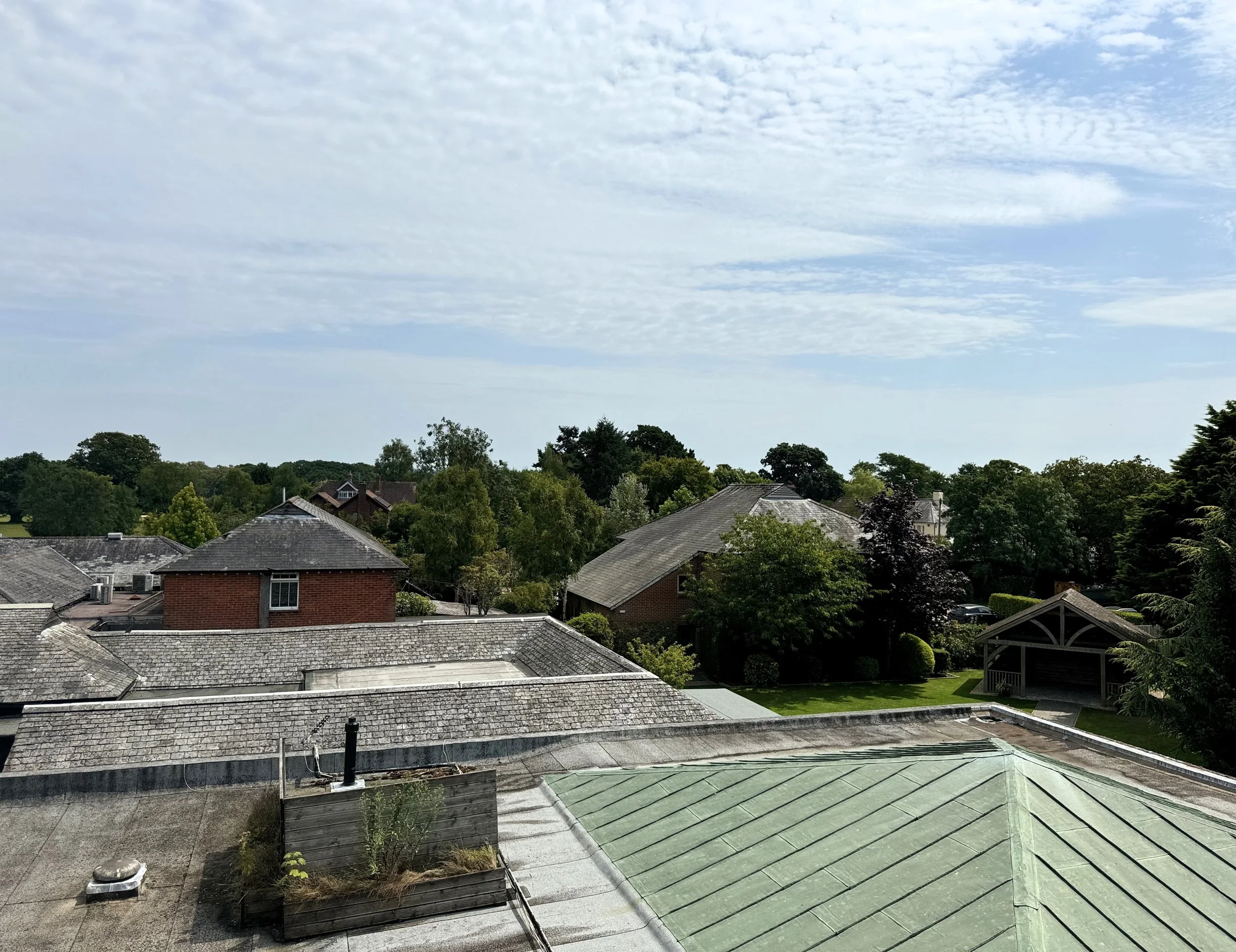 View of rooftops in a suburban neighborhood with trees, houses, and a partly cloudy sky.