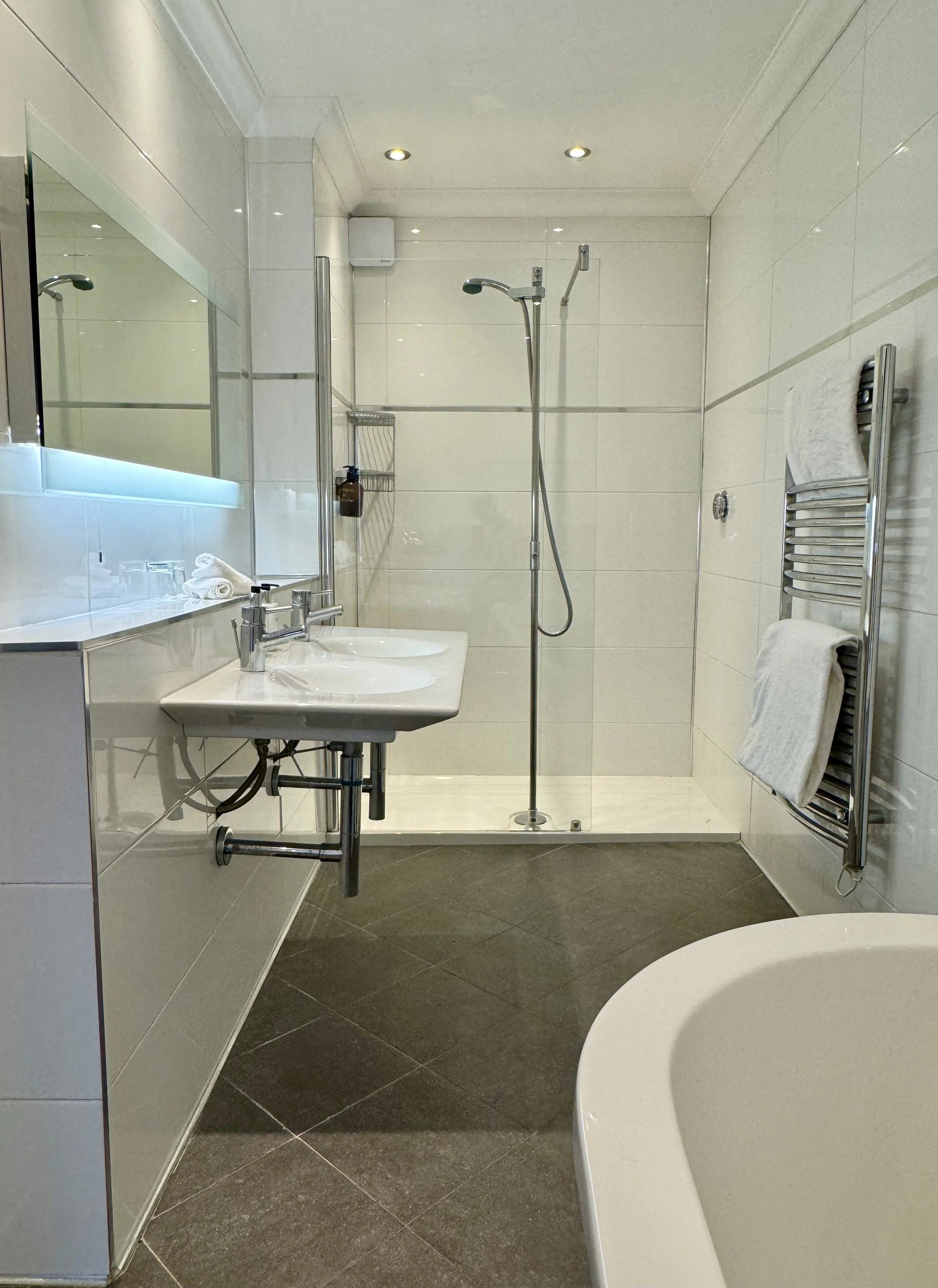 Modern bathroom with double sink vanity, mirror, towel rack, walk-in shower with glass door, and a partial view of a bathtub.